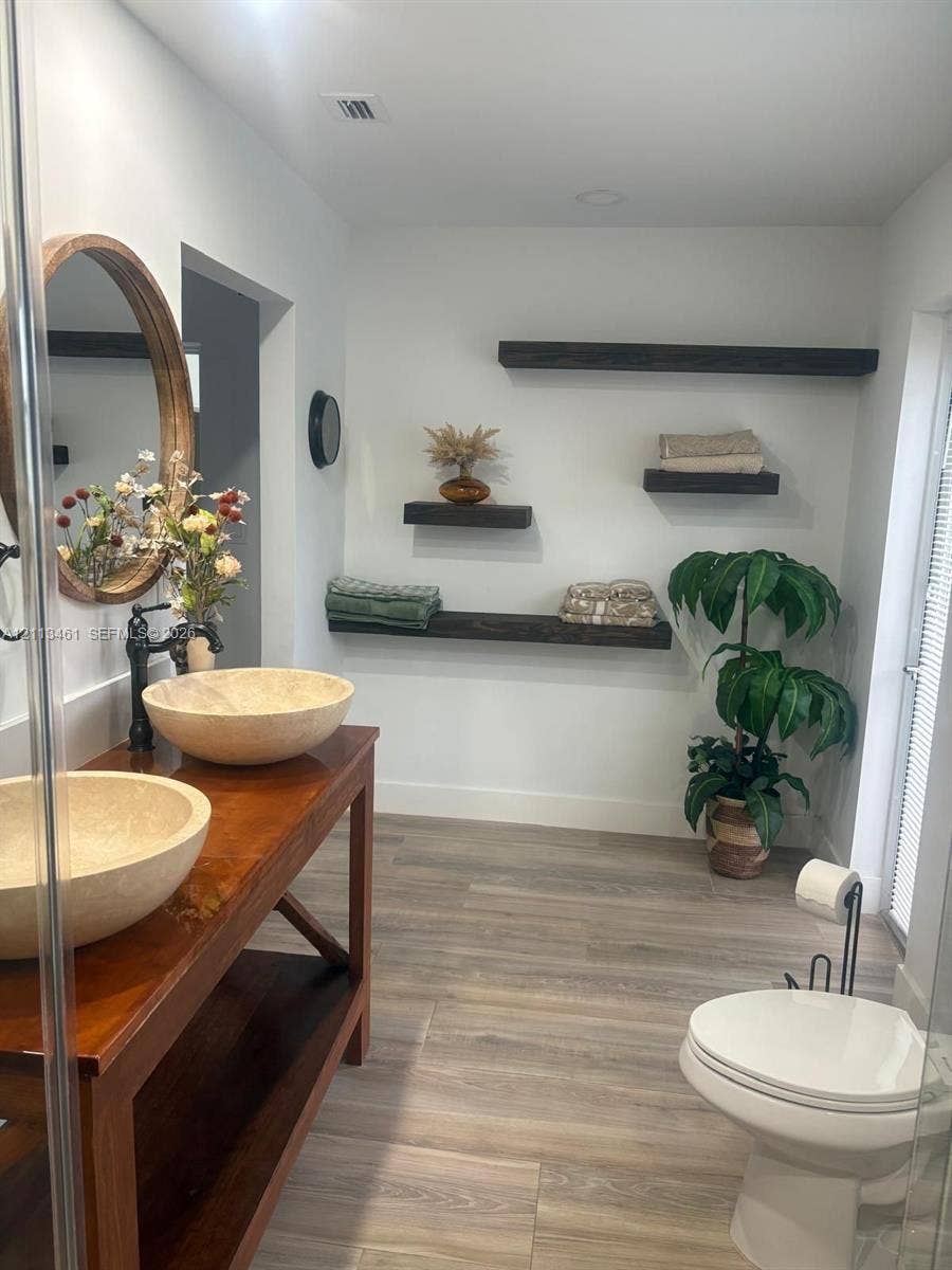 9961 SW 20th Street, Miami, Miami, FL 33165 Double-basin vanity with vessel sinks, wood-finish flooring, and floating wall-mounted shelving