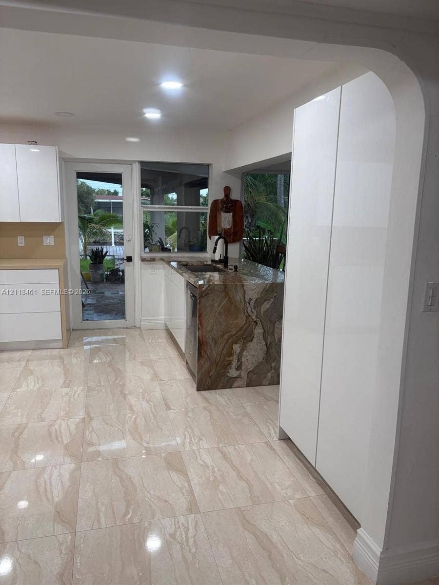9961 SW 20th Street, Miami, Miami, FL 33165 Kitchen featuring white slab-front cabinetry, stone-surface counters with a waterfall edge, large-format tile flooring, and a glass-paneled exterior door