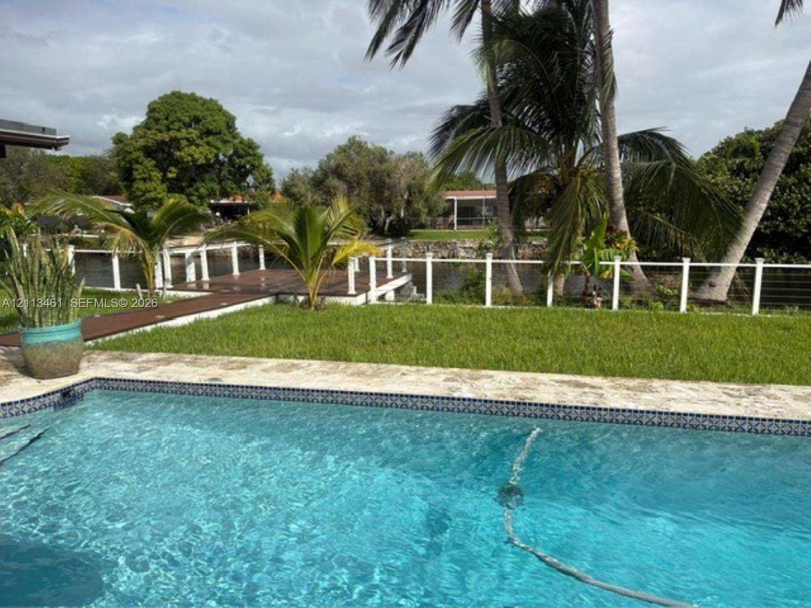 9961 SW 20th Street, Miami, Miami, FL 33165 Swimming pool with stone surround, waterfront wooden deck, white railing, and mature landscaping