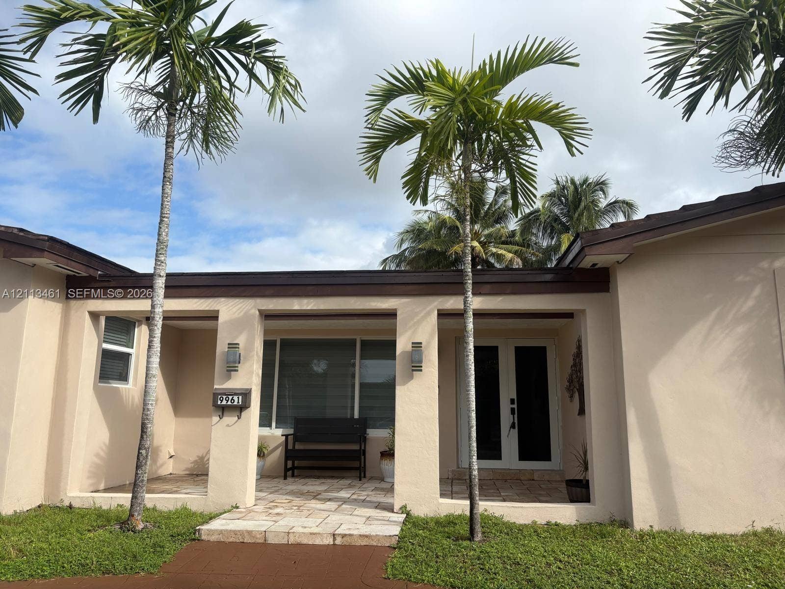 9961 SW 20th Street, Miami, Miami, FL 33165 Stucco exterior facade featuring a covered entryway, stone paver porch, dual entry doors, and wall-mounted exterior lighting fixtures