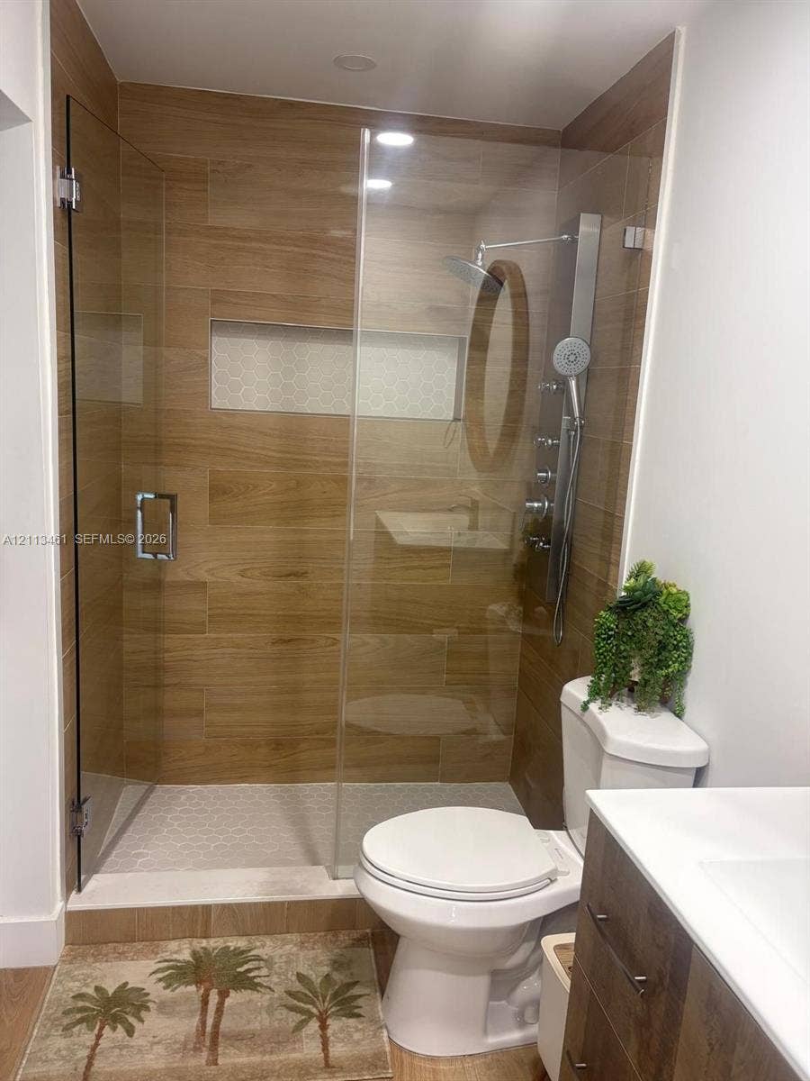 9961 SW 20th Street, Miami, Miami, FL 33165 Walk-in shower featuring wood-finish tile surround, integrated mosaic niche, frameless glass enclosure, and multi-function shower system with handheld wand, paired with a wood-finish vanity and white countertop