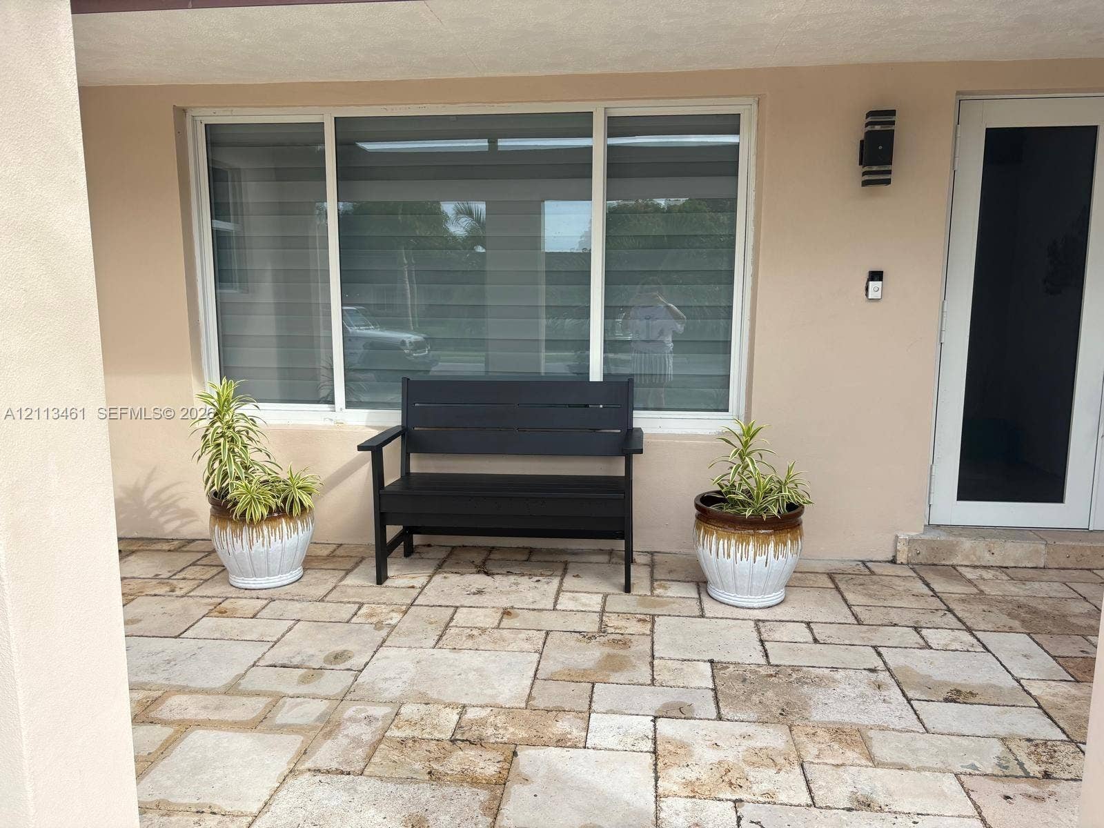 9961 SW 20th Street, Miami, Miami, FL 33165 Covered entrance featuring stone paver flooring, a large multi-pane window with integrated blinds, and an exterior wall-mounted light fixture