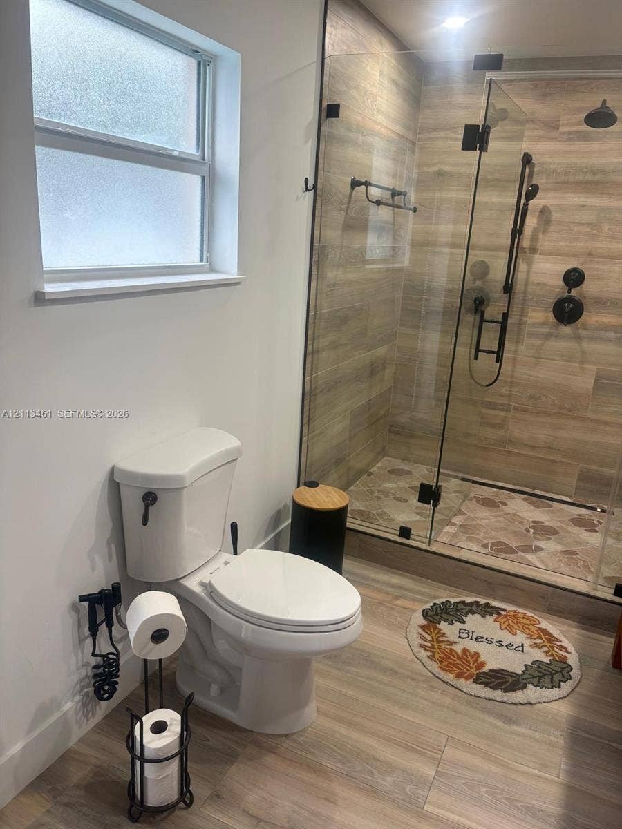 9961 SW 20th Street, Miami, Miami, FL 33165 Walk-in shower featuring glass enclosure, wood-finish wall tile, and matte black fixtures, paired with wood-finish flooring and privacy-glass window