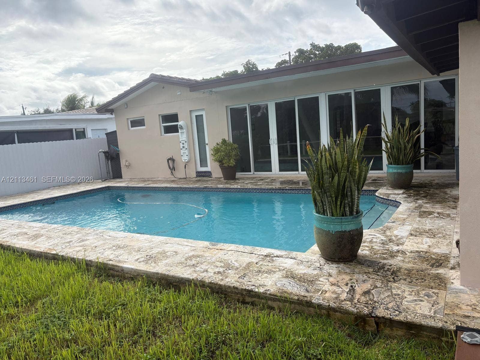 9961 SW 20th Street, Miami, Miami, FL 33165 In-ground swimming pool with stone-surfaced deck, white multi-panel sliding glass doors, and perimeter privacy fencing