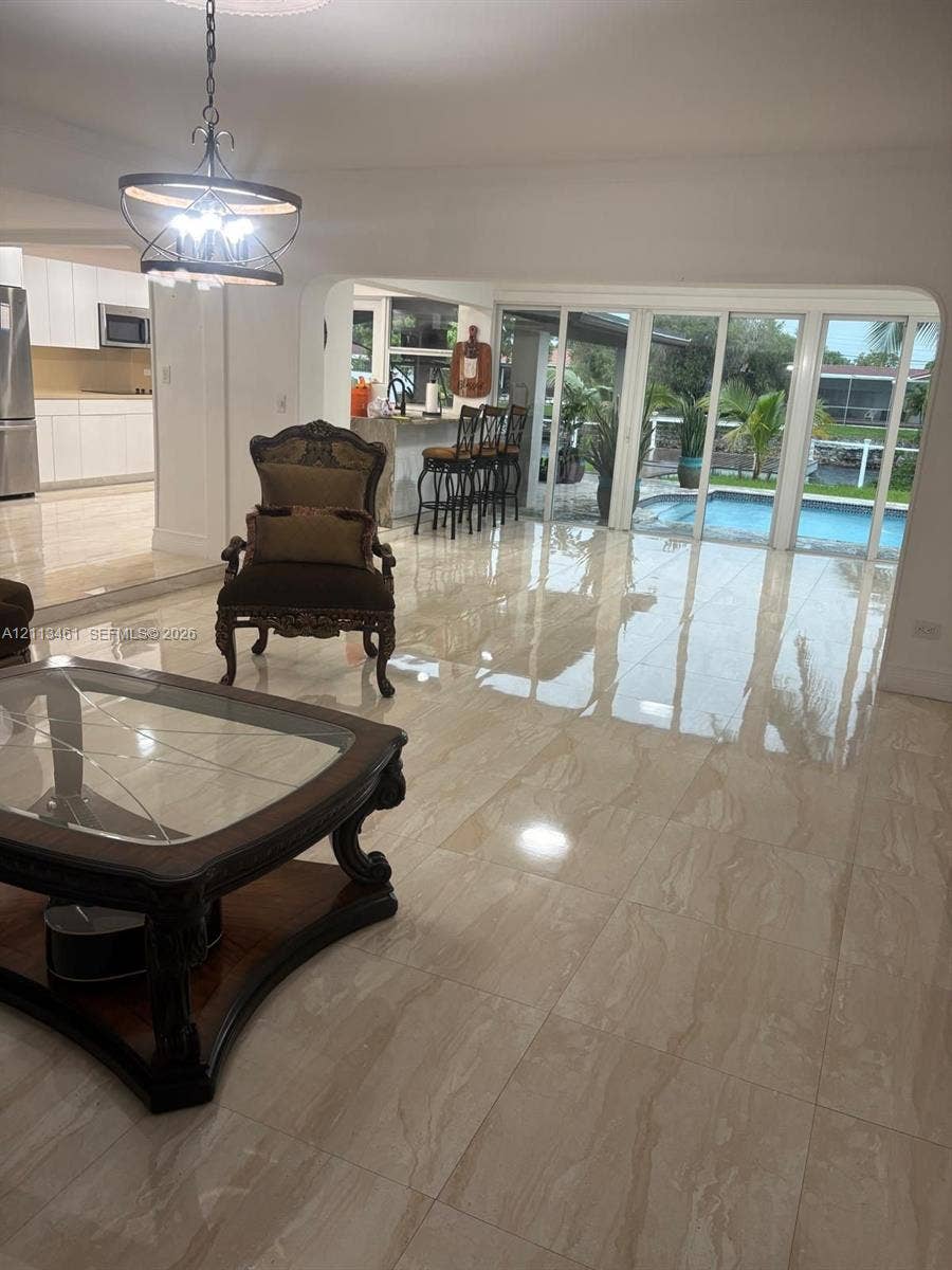9961 SW 20th Street, Miami, Miami, FL 33165 Open-concept living space featuring large-format tile flooring, a multi-panel sliding glass door, a built-in kitchen breakfast bar, and a decorative metal chandelier