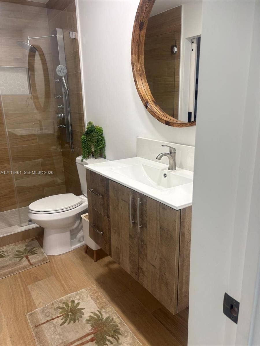 9961 SW 20th Street, Miami, Miami, FL 33165 Floating vanity with wood-finish cabinetry, integrated white countertop, walk-in shower with wood-finish tile surround, and circular wall-mounted mirror