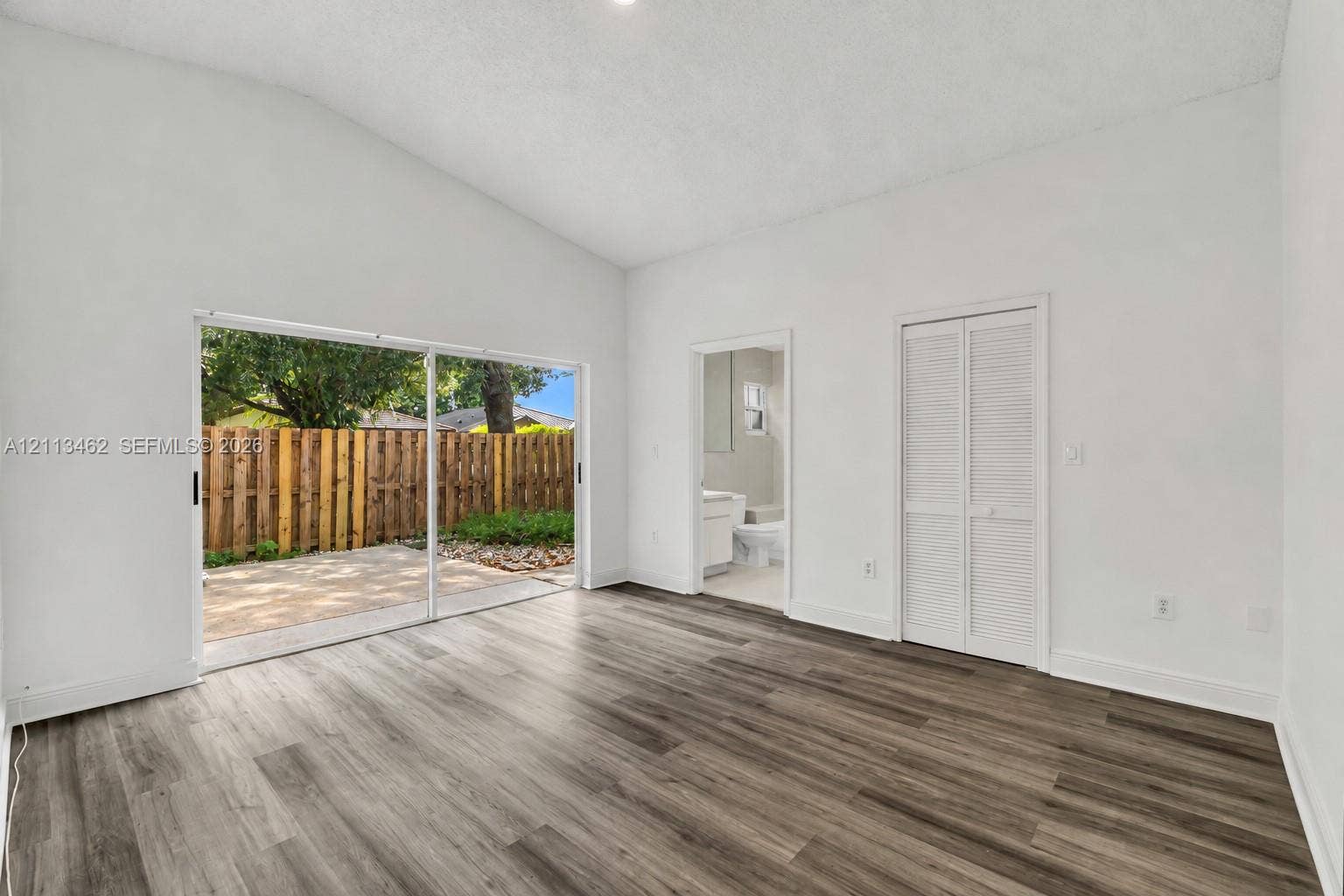 Vaulted ceiling, wood-finish flooring, sliding glass door, and louvered closet doors