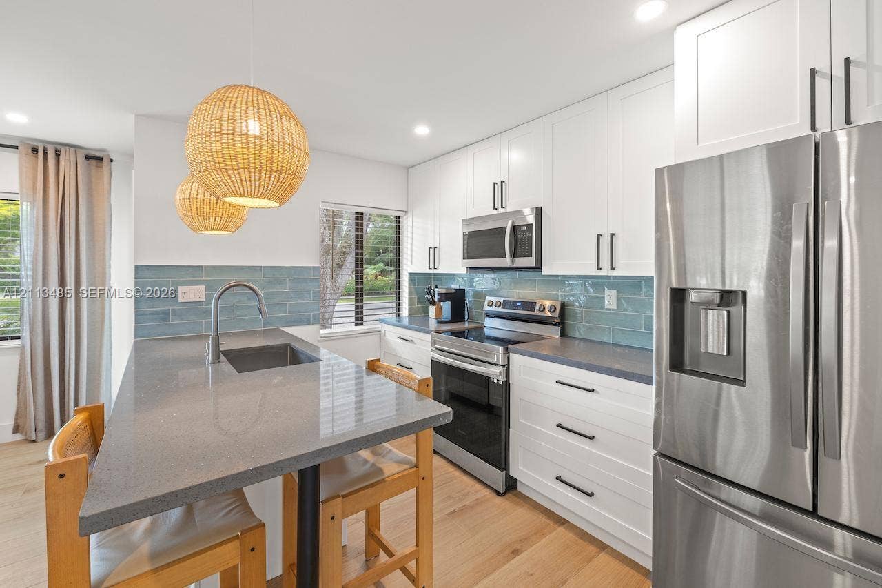 1505 SW 32nd Court, #1, Fort Lauderdale, Fort Lauderdale, FL 33315 Kitchen featuring white cabinetry, grey stone-finish countertops, blue tile backsplash, stainless steel appliances, and wood-finish flooring