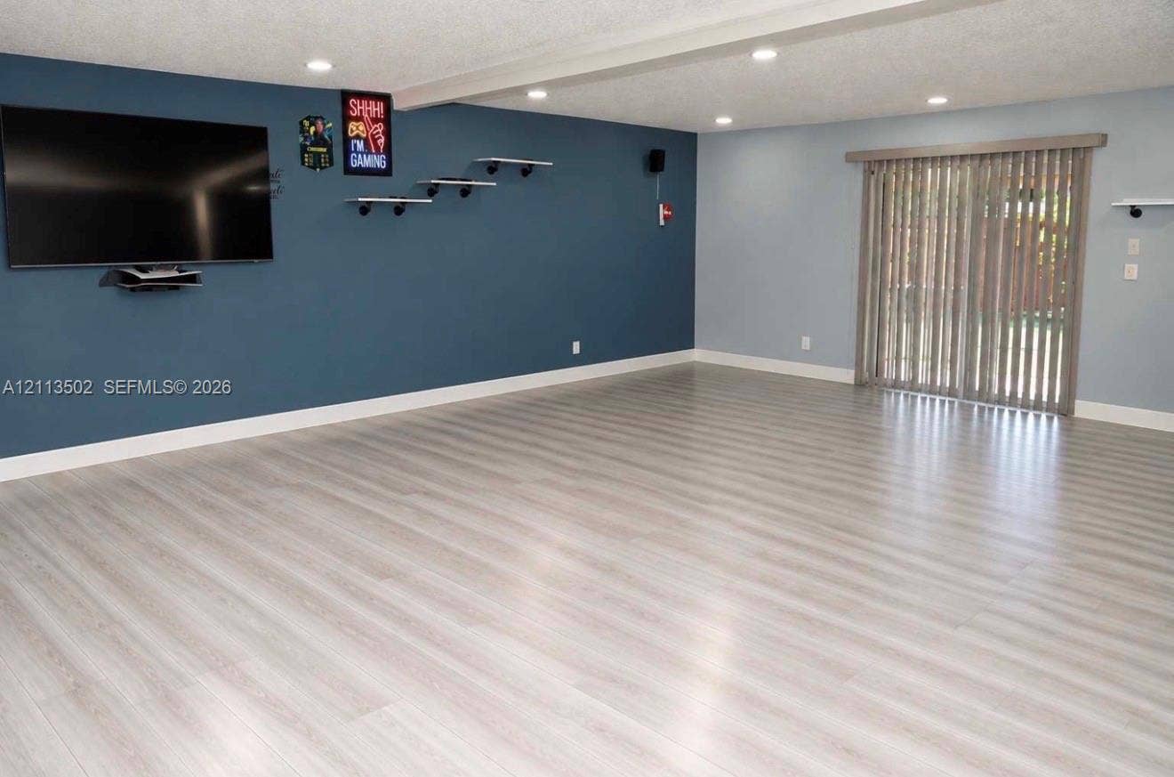 4332 NW 3 Terrace, Deerfield Beach, Deerfield Beach, FL 33064 Interior space featuring wood-finish flooring, recessed lighting, a dark-toned accent wall with wall-mounted shelving, and sliding glass doors with vertical blinds
