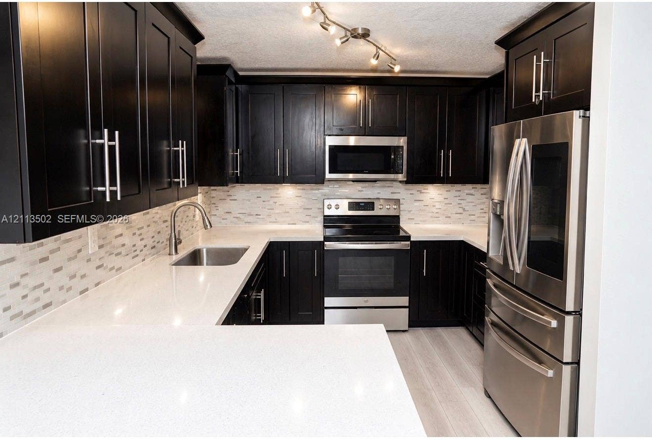 4332 NW 3 Terrace, Deerfield Beach, Deerfield Beach, FL 33064 Kitchen featuring dark shaker-style cabinetry, white quartz countertops, multi-toned linear tile backsplash, stainless steel appliances, and track lighting