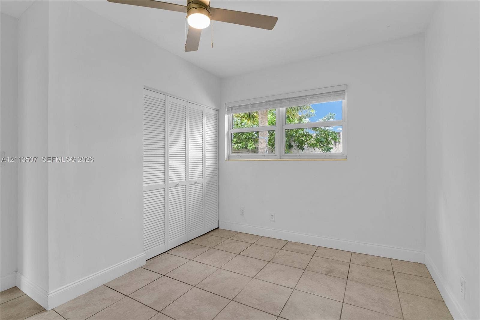 Tile flooring, built-in louvered-panel closet doors, and a ceiling fan with integrated lighting