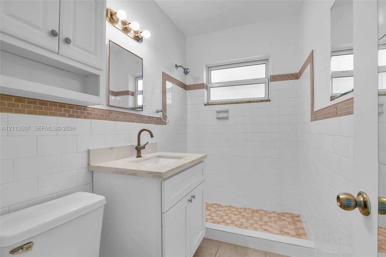Bathroom featuring white subway tile walls with decorative mosaic inlay, a walk-in shower with mosaic tile flooring, a white vanity with a neutral-toned countertop, and a wall-mounted vanity light fixture