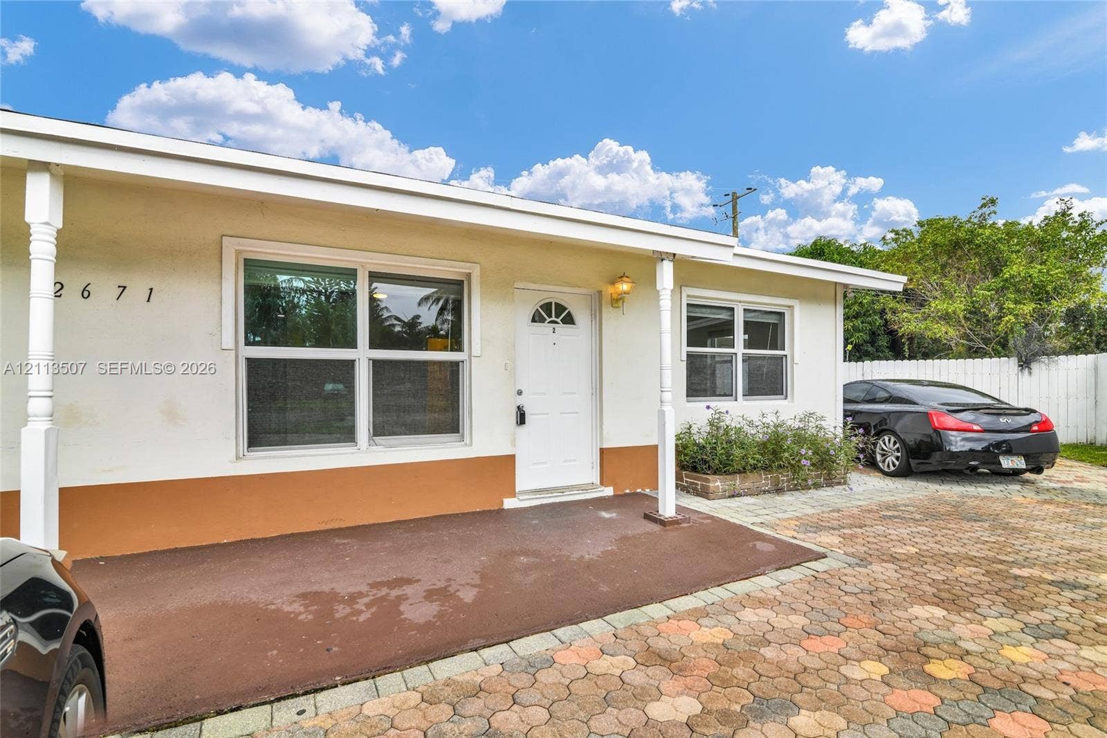 Exterior facade featuring stucco siding, a covered front porch, multi-pane windows, and a paved brick driveway
