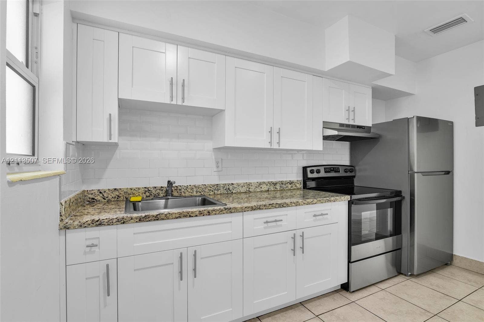 Kitchen featuring white shaker-style cabinetry, stone-finish countertops, subway tile backsplash, stainless steel appliances, and tile flooring