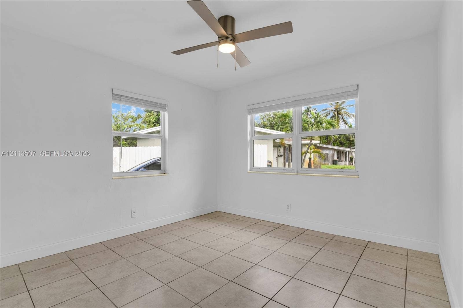 Neutral-toned ceramic tile flooring, metallic ceiling fan with integrated lighting, and dual windows with horizontal blinds