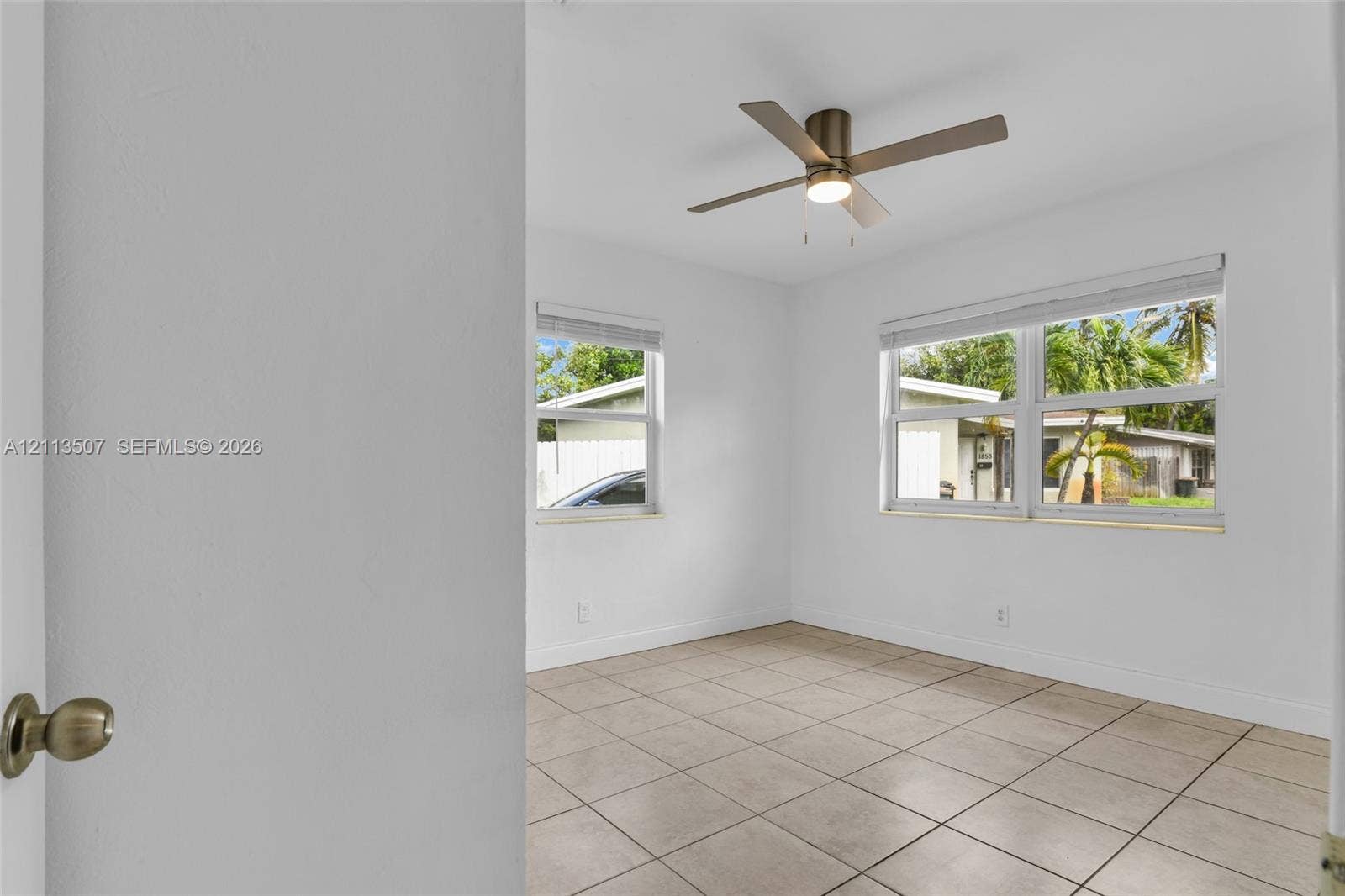 Neutral-toned ceramic tile flooring, clean white walls, multi-pane windows with horizontal blinds, and a modern brushed-finish ceiling fan with integrated lighting