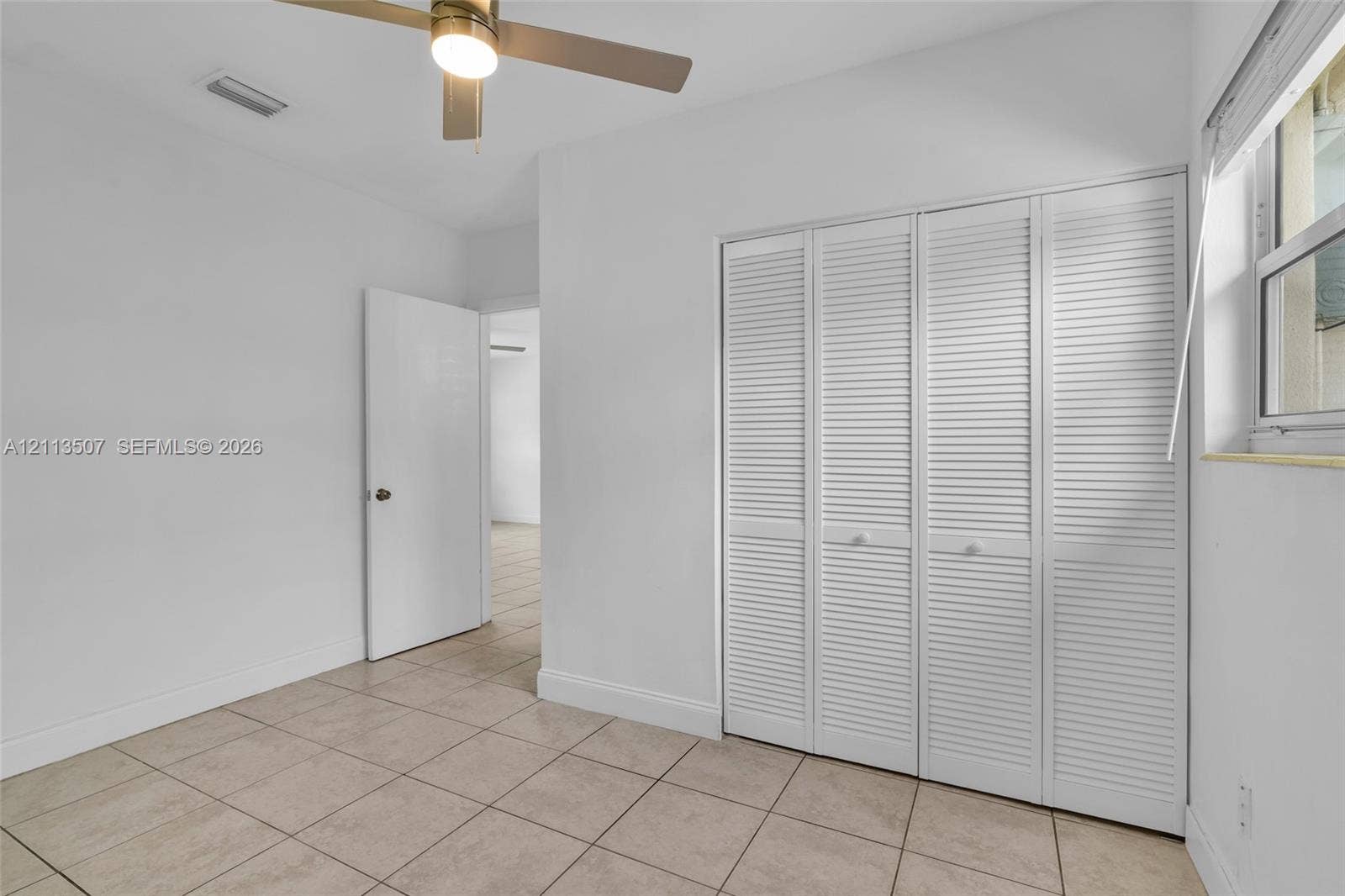 Neutral interior featuring large-format tile flooring, a ceiling fan with integrated lighting, and a closet with white louvered bi-fold doors