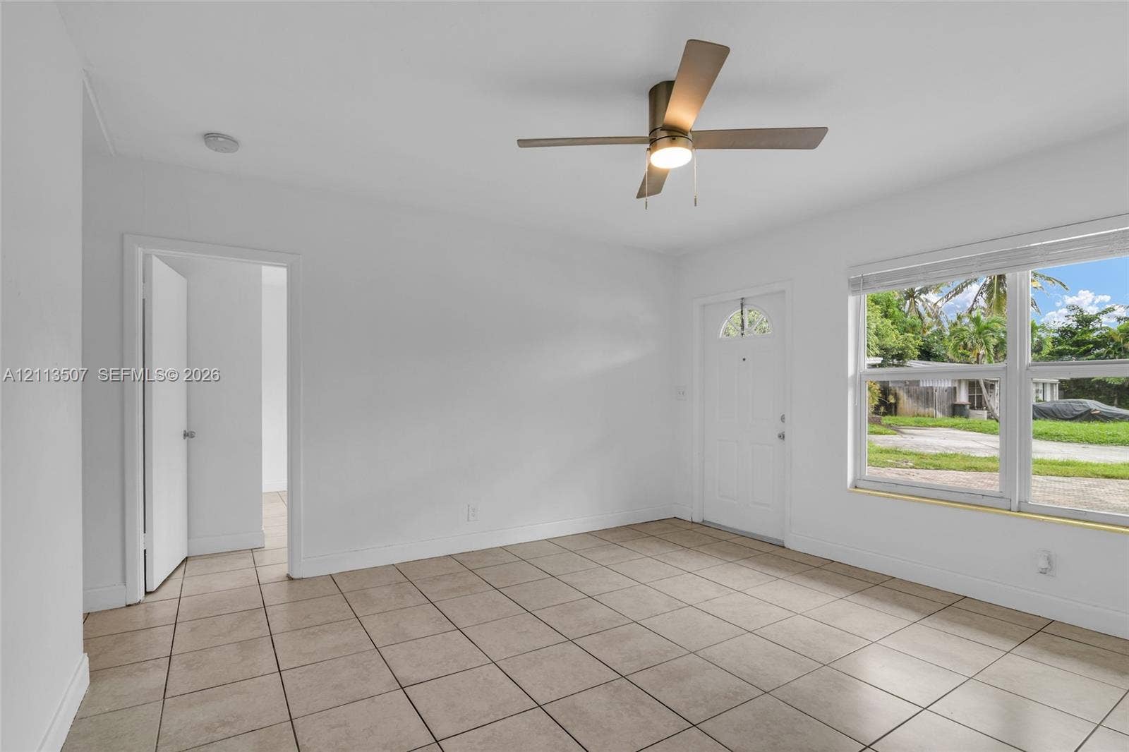 Neutral-toned tile flooring, minimalist white walls, ceiling-mounted fan with integrated lighting, and white exterior door with glass insert