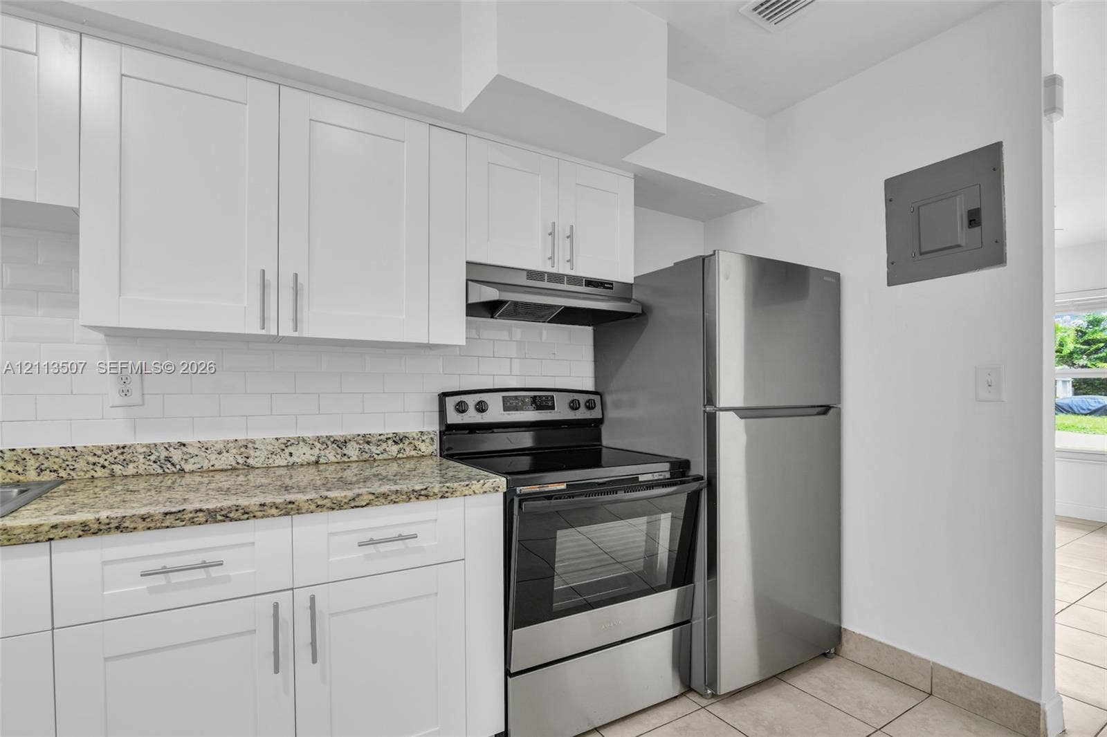 Kitchen featuring white Shaker-style cabinetry, stone countertops, a white subway tile backsplash, and stainless steel appliances