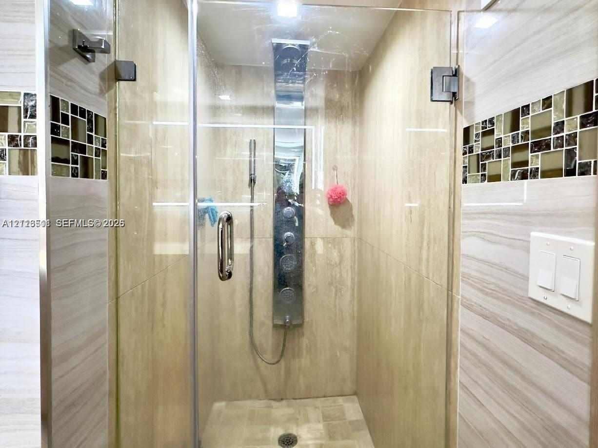 1201 S Ocean Drive, #2202S, Hollywood, FL 33019 Walk-in shower featuring a frameless glass door, wall-mounted body spray panel, large-format tile surround, and decorative mosaic tile inlay