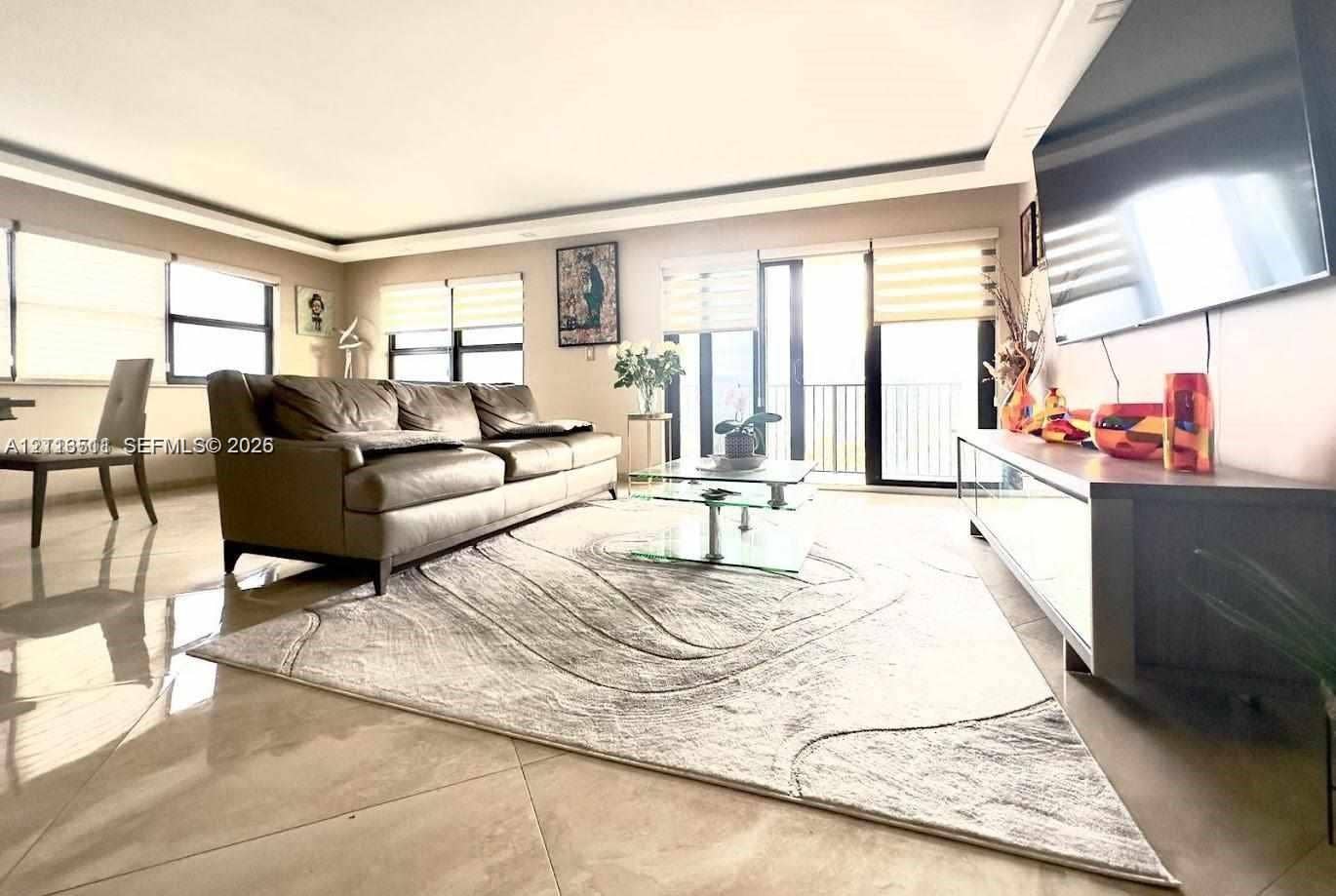 1201 S Ocean Drive, #2202S, Hollywood, FL 33019 Living space featuring large-format tile flooring, recessed tray ceiling, multiple floor-to-ceiling windows with integrated roller shades, and sliding glass doors with balcony access