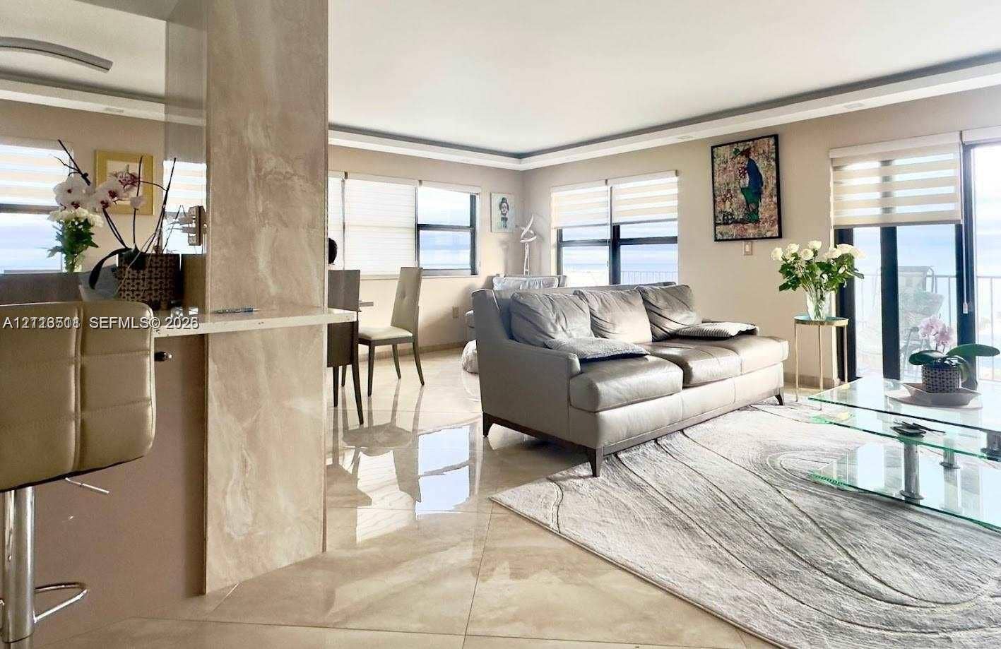 1201 S Ocean Drive, #2202S, Hollywood, FL 33019 Open-concept living space featuring large-format polished tile flooring, natural stone-faced breakfast bar, recessed tray ceiling, and expansive windows with custom roller shades