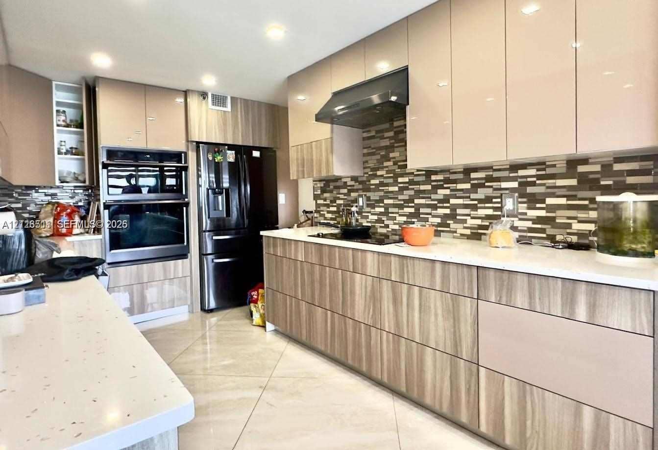 1201 S Ocean Drive, #2202S, Hollywood, FL 33019 Kitchen featuring high-gloss cabinetry with wood-finish lower panels, solid surface countertops, a mosaic tile backsplash, and built-in double ovens