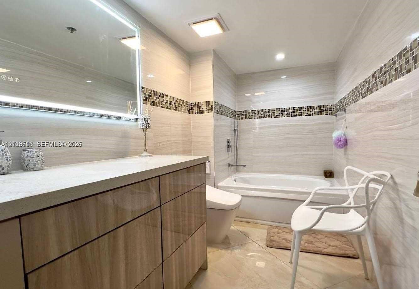 1201 S Ocean Drive, #2202S, Hollywood, FL 33019 Bathroom featuring a gloss-finish wood cabinetry vanity, quartz countertop, illuminated wall mirror, integrated tile mosaic accents, and tile flooring
