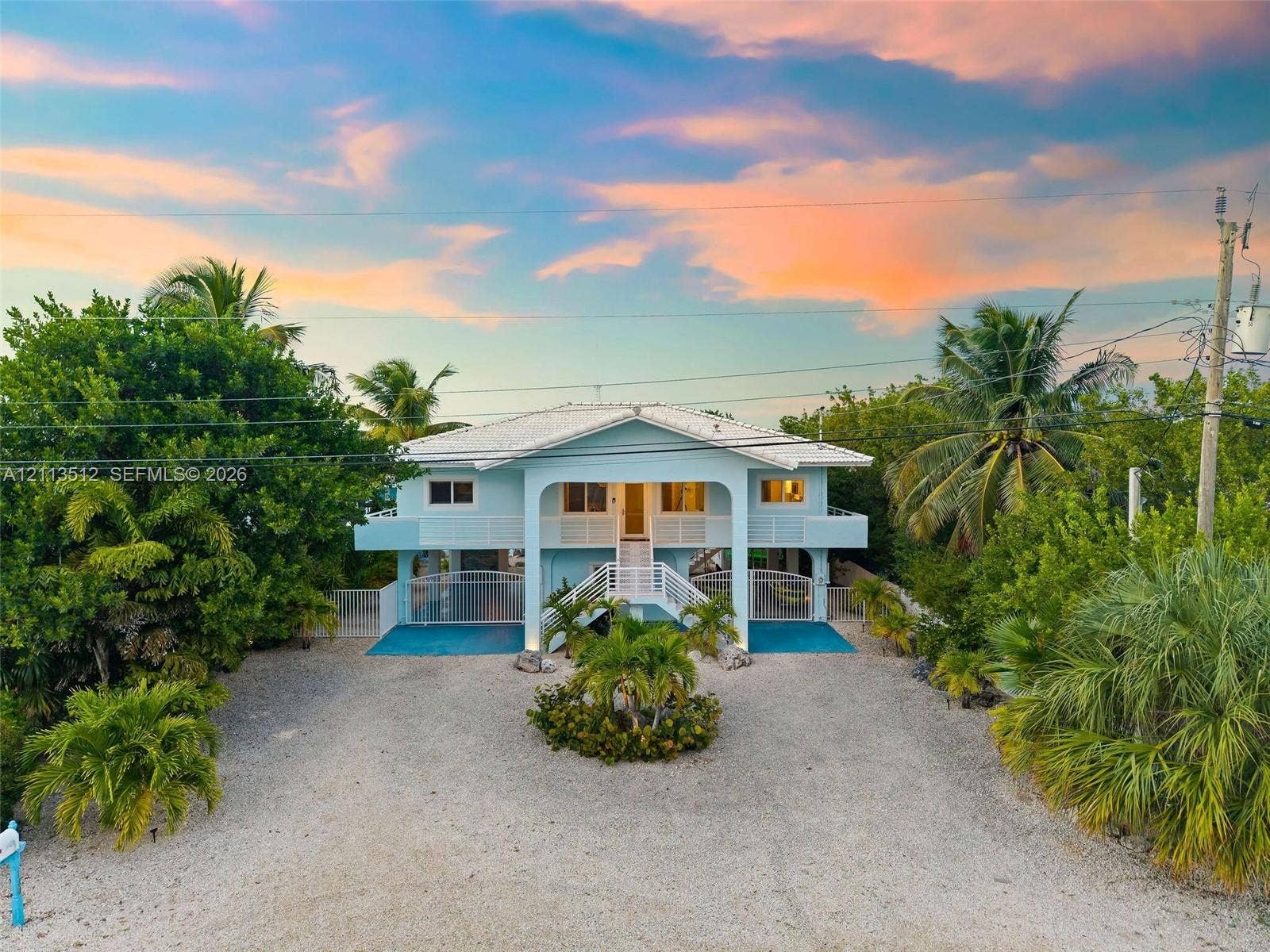 Key Largo, FL 33037 Elevated home featuring a metal roof, wraparound balcony, concrete staircase, and a gravel driveway
