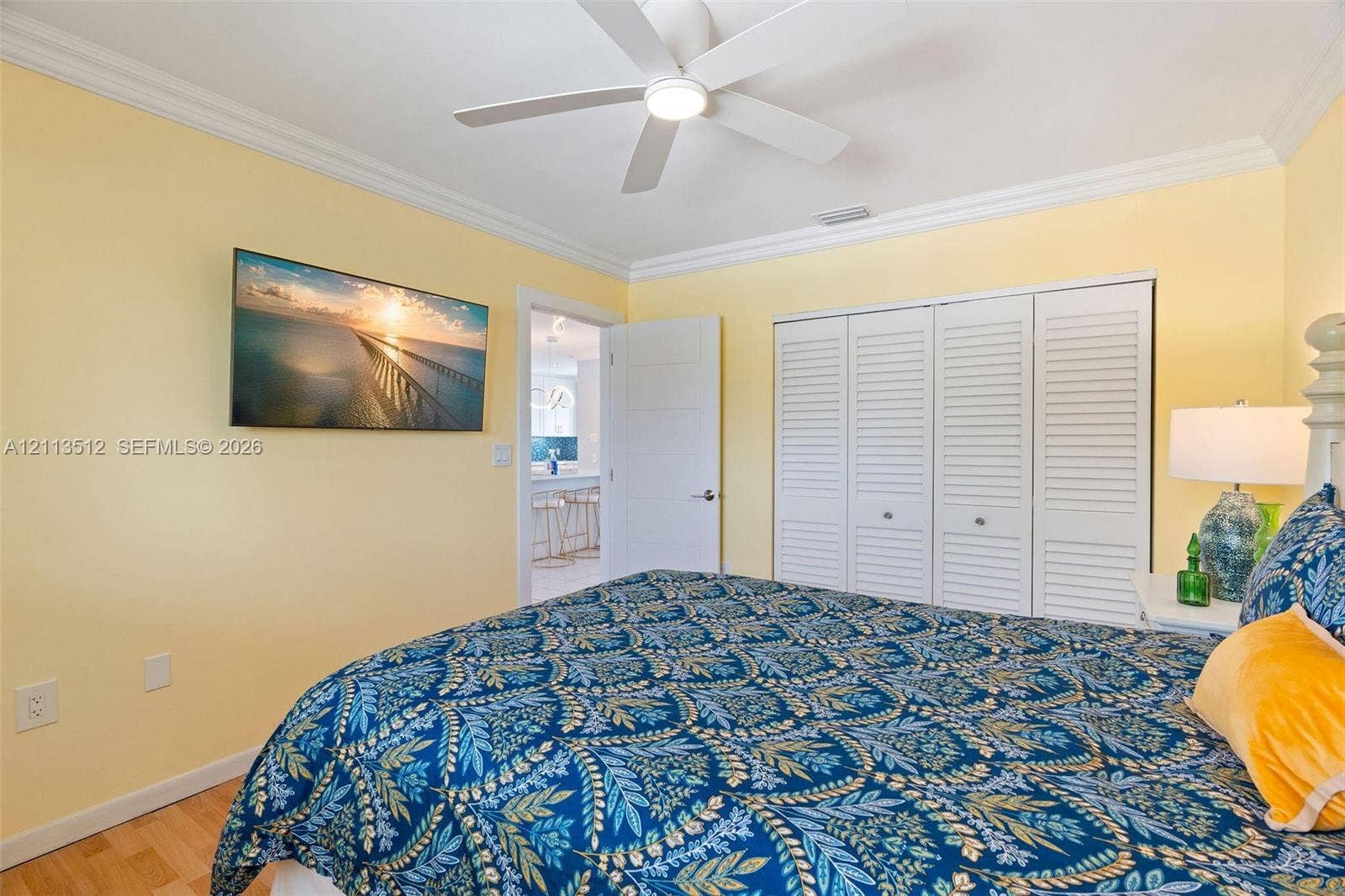 Key Largo, FL 33037 Room featuring white crown molding, a ceiling-mounted fan with integrated lighting, wood-finish flooring, and a triple-panel louvered closet door