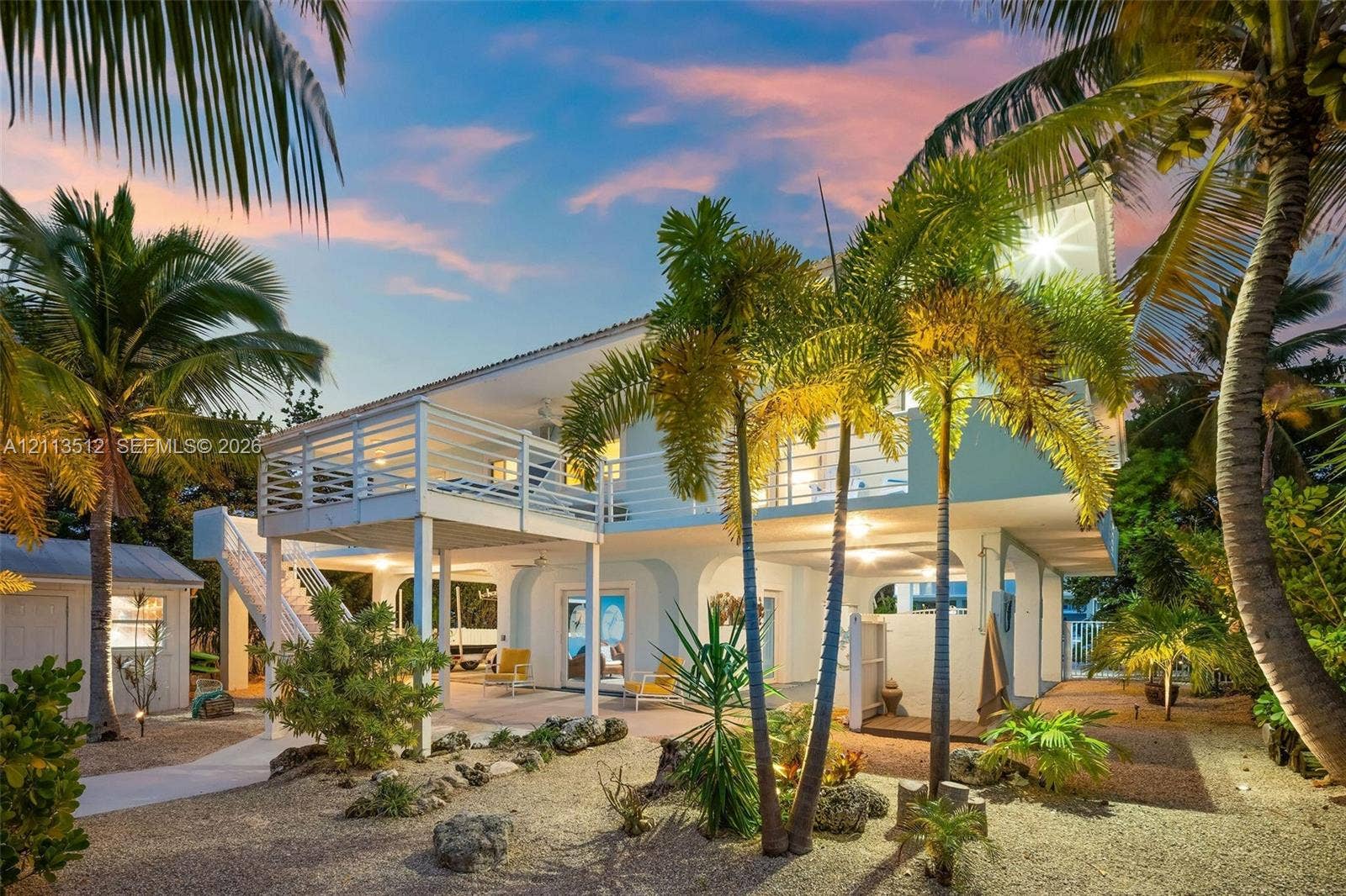 Key Largo, FL 33037 Elevated residence featuring a wrap-around balcony, arched ground-level architecture, external staircase, and tropical landscaping