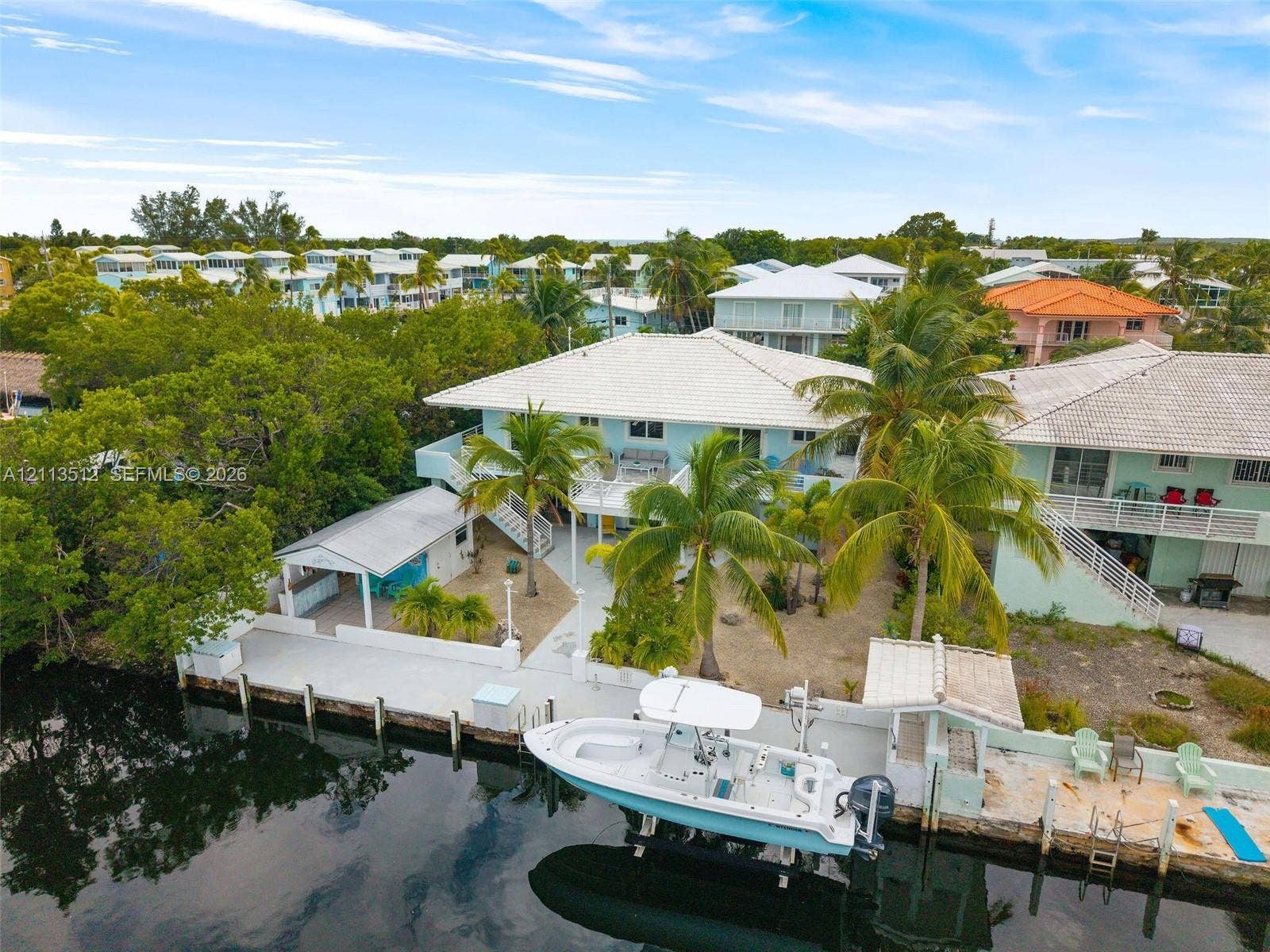 Key Largo, FL 33037 Waterfront property featuring a private boat dock, concrete bulkhead, covered outdoor living structure, and mature palm trees