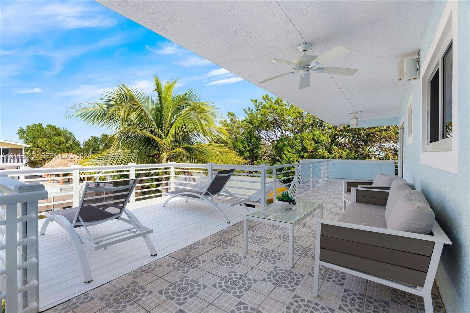 Key Largo, FL 33037 Covered balcony featuring white deck flooring, geometric patterned tile, white metal railings, and a ceiling-mounted fan