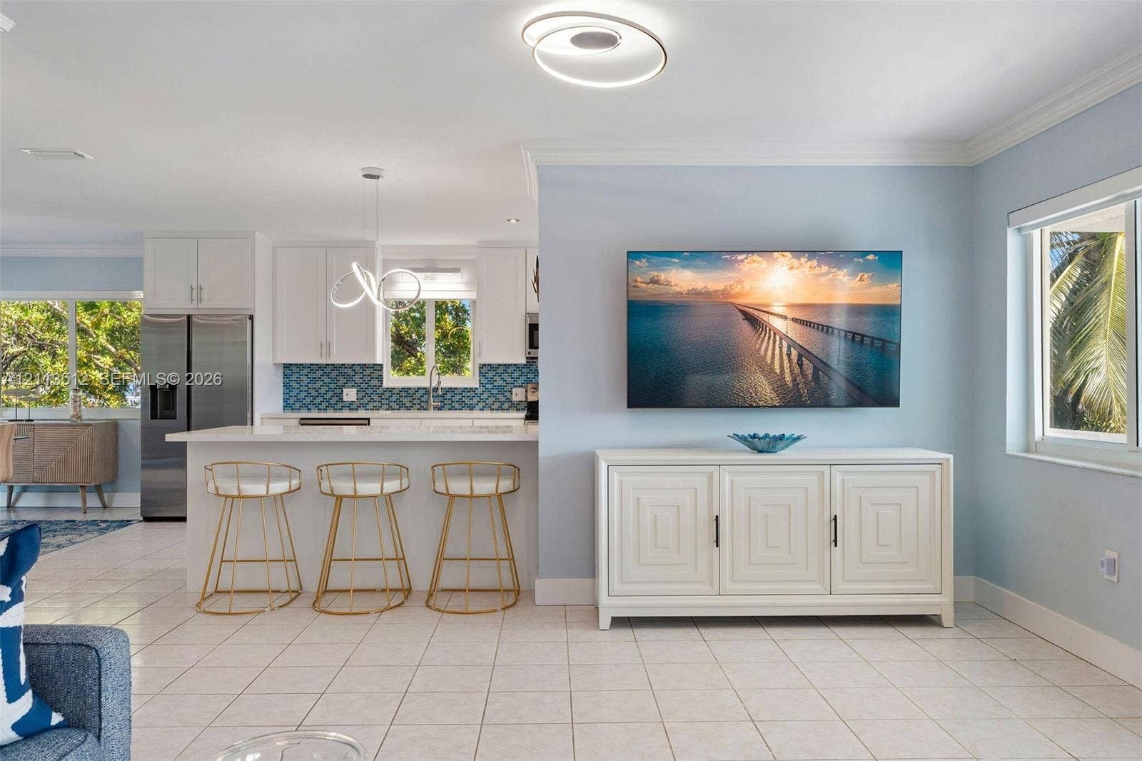 Key Largo, FL 33037 Open-concept interior featuring a kitchen with white cabinetry, a breakfast bar with geometric tile backsplash, stainless steel appliances, circular LED lighting fixtures, and tile flooring