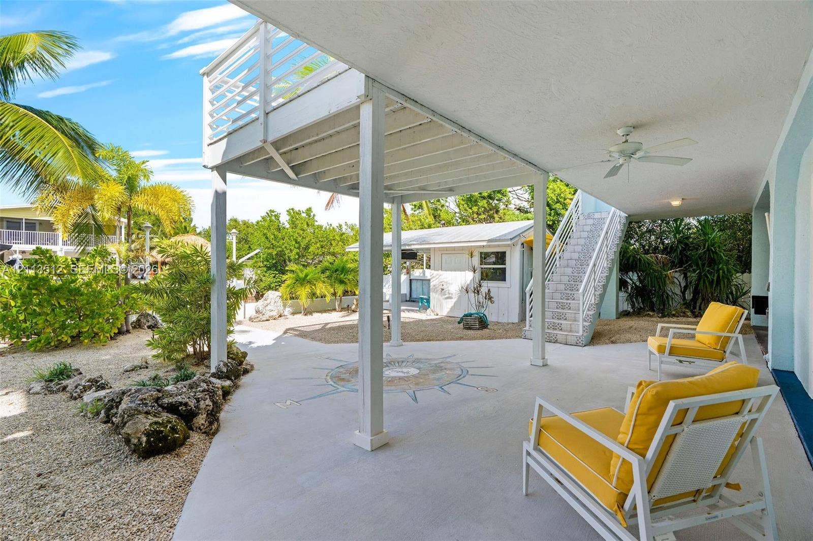 Key Largo, FL 33037 Covered ground-level patio featuring a decorative nautical compass inlay, elevated upper balcony, integrated ceiling fan, and staircase with metal railings