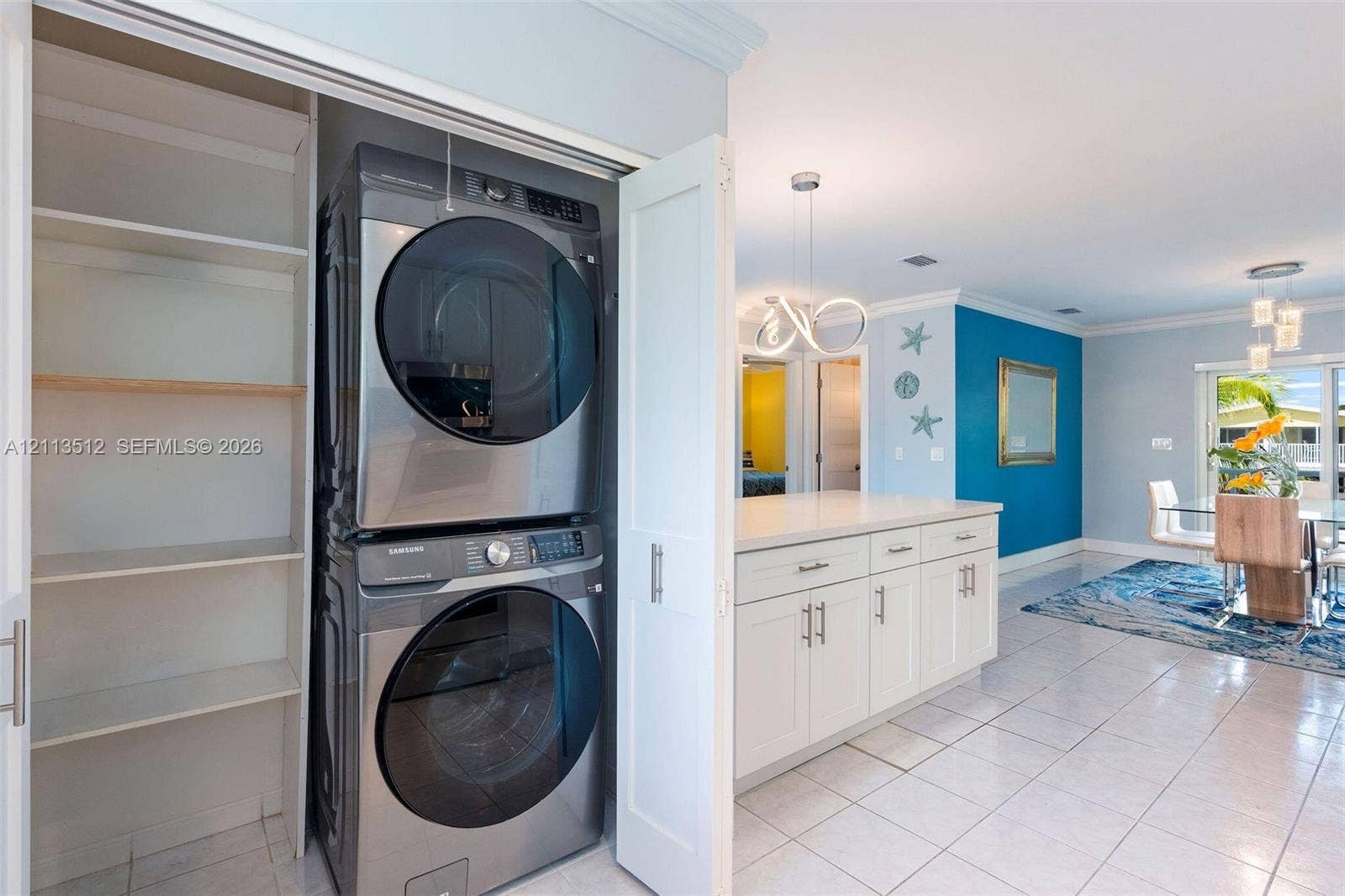 Key Largo, FL 33037 Laundry area featuring a stacked stainless steel washer and dryer, built-in shelving, white cabinetry with stone countertops, and tile flooring