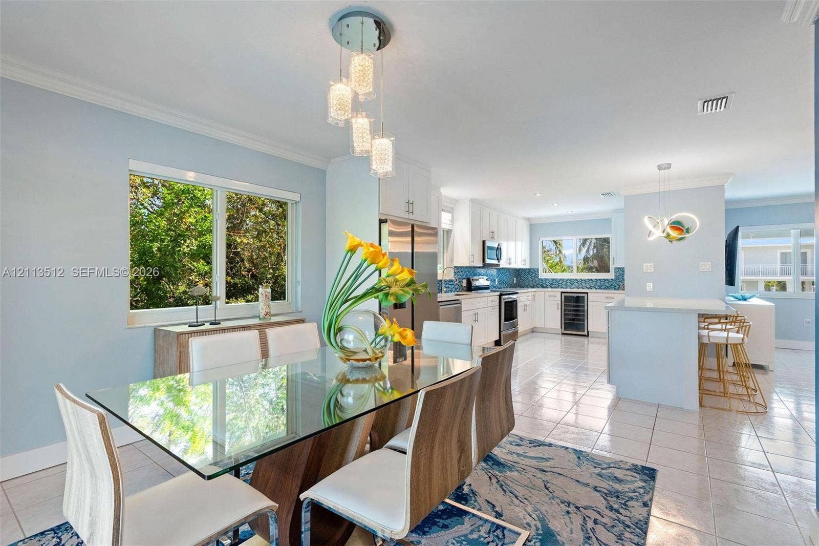 Key Largo, FL 33037 Open-concept kitchen and dining area featuring white shaker-style cabinetry, a central island with bar seating, tile flooring, and multi-light geometric pendant fixtures