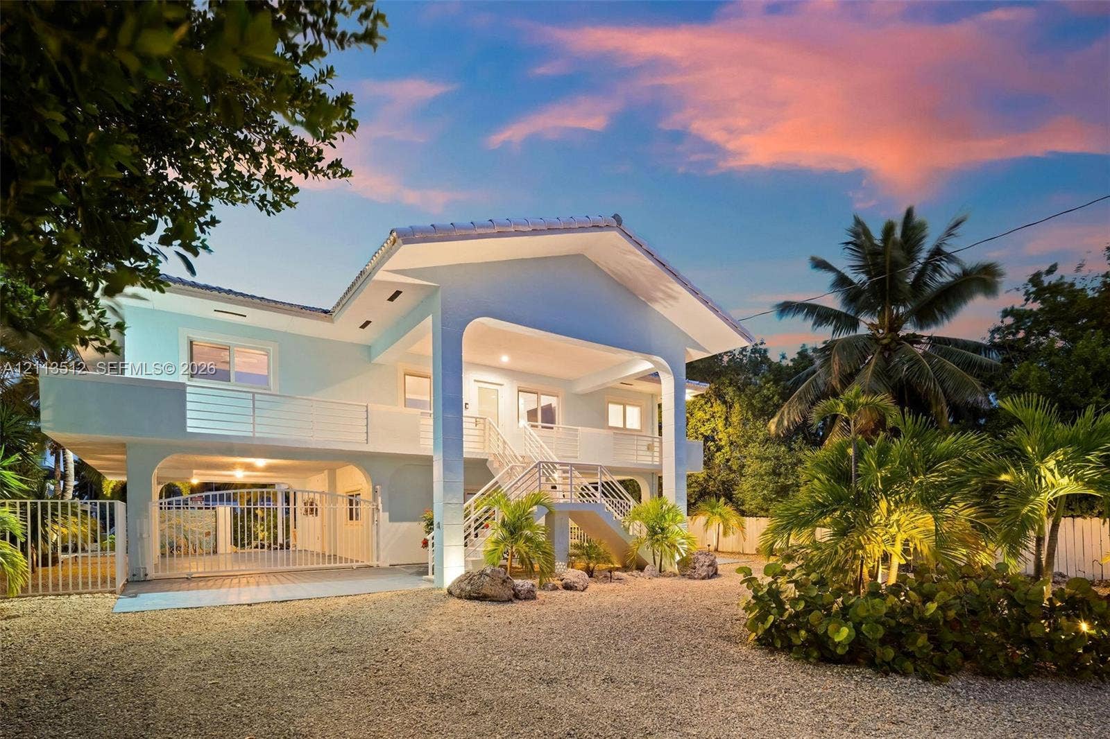Key Largo, FL 33037 Elevated residence featuring a covered entryway, second-story balcony with metal railings, arched architectural detailing, and a ground-level gated carport