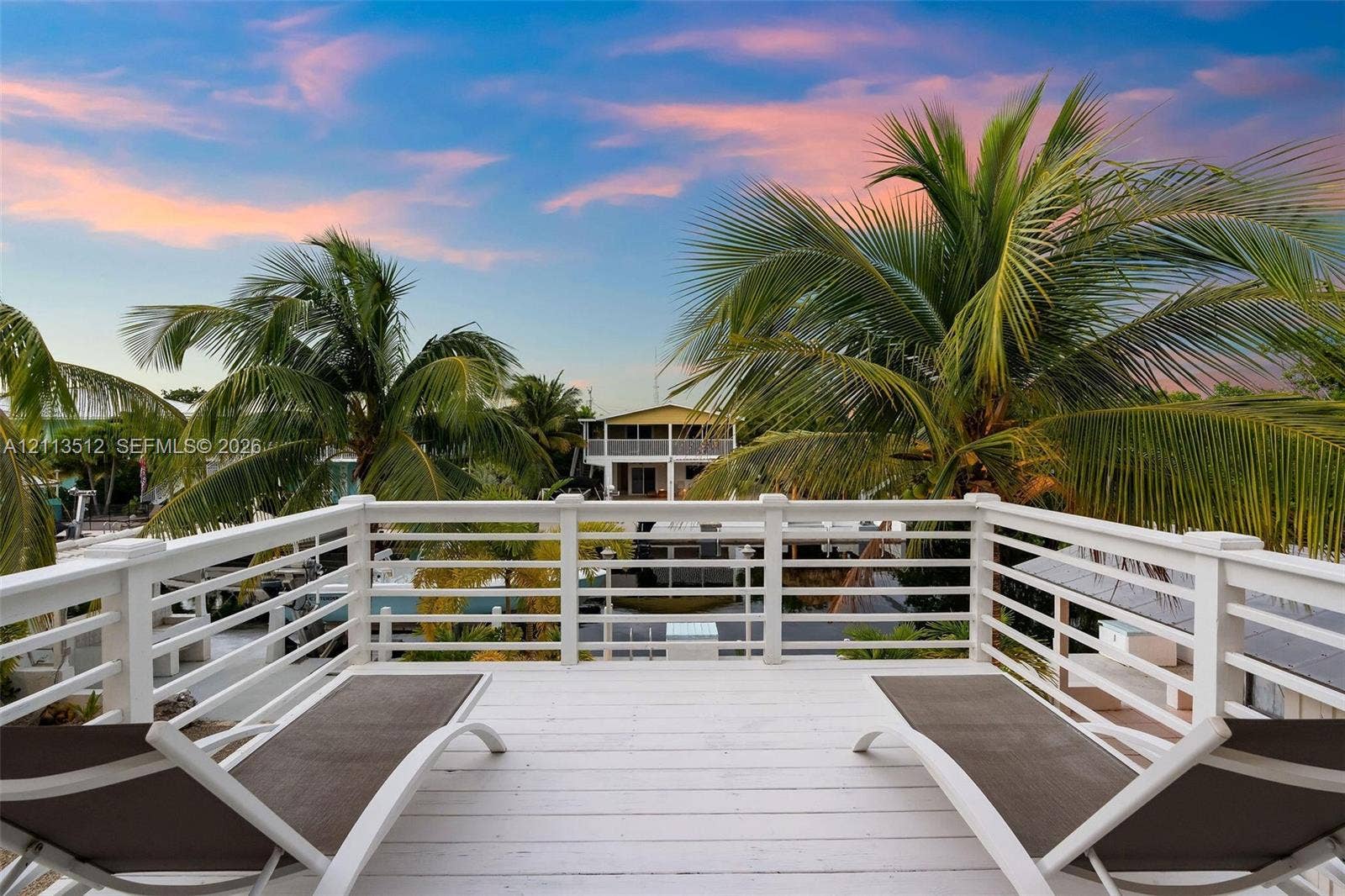 Key Largo, FL 33037 Elevated deck with white horizontal railing and wood-plank flooring, accented by mature palm trees