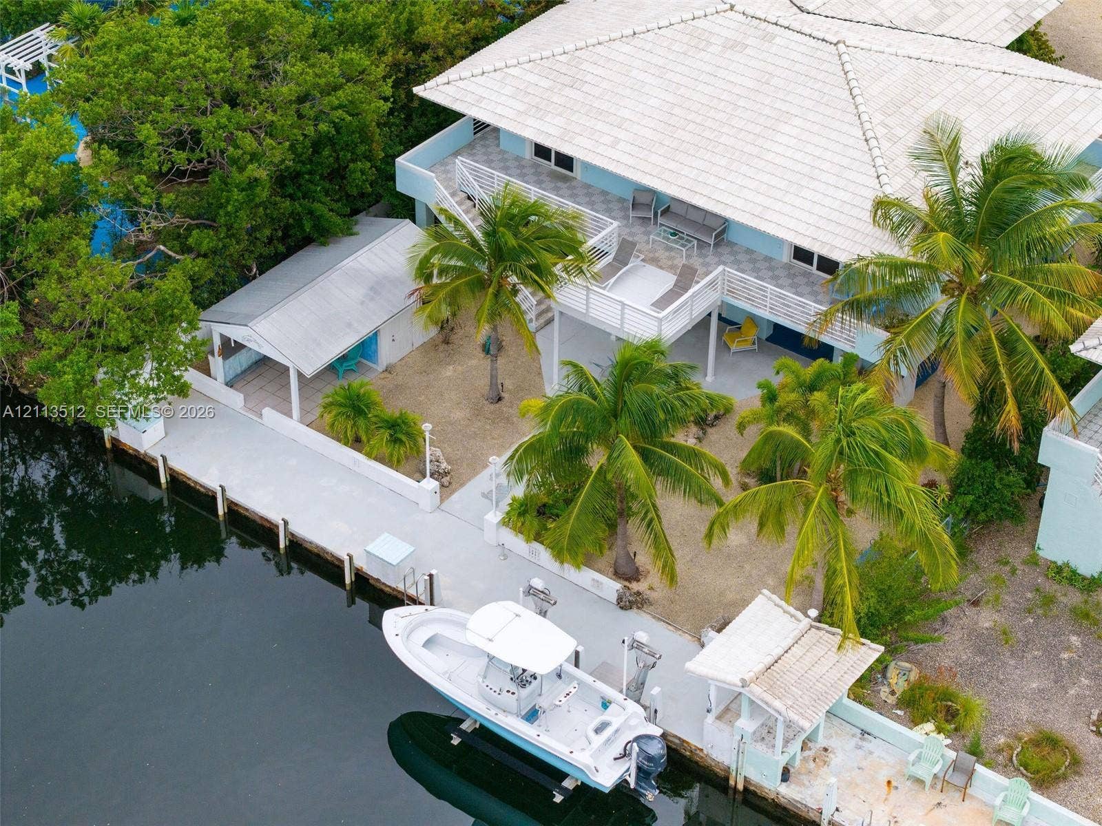 Key Largo, FL 33037 Waterfront property featuring a private concrete dock with boat lift, covered outdoor pavilion, elevated wrap-around balcony, and tile roof