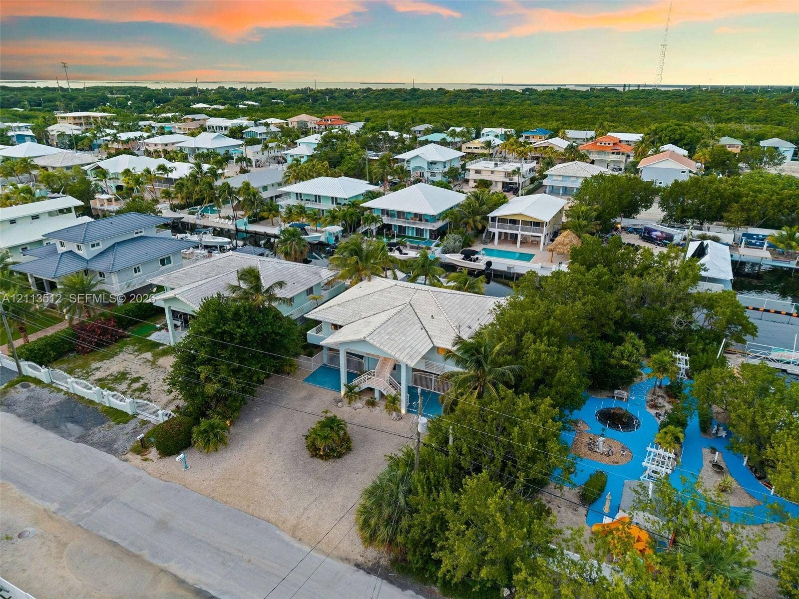 Key Largo, FL 33037 Elevated coastal residence featuring a metal roof, concrete-finish parking area, mature landscaping, and a blue-surfaced outdoor recreational space