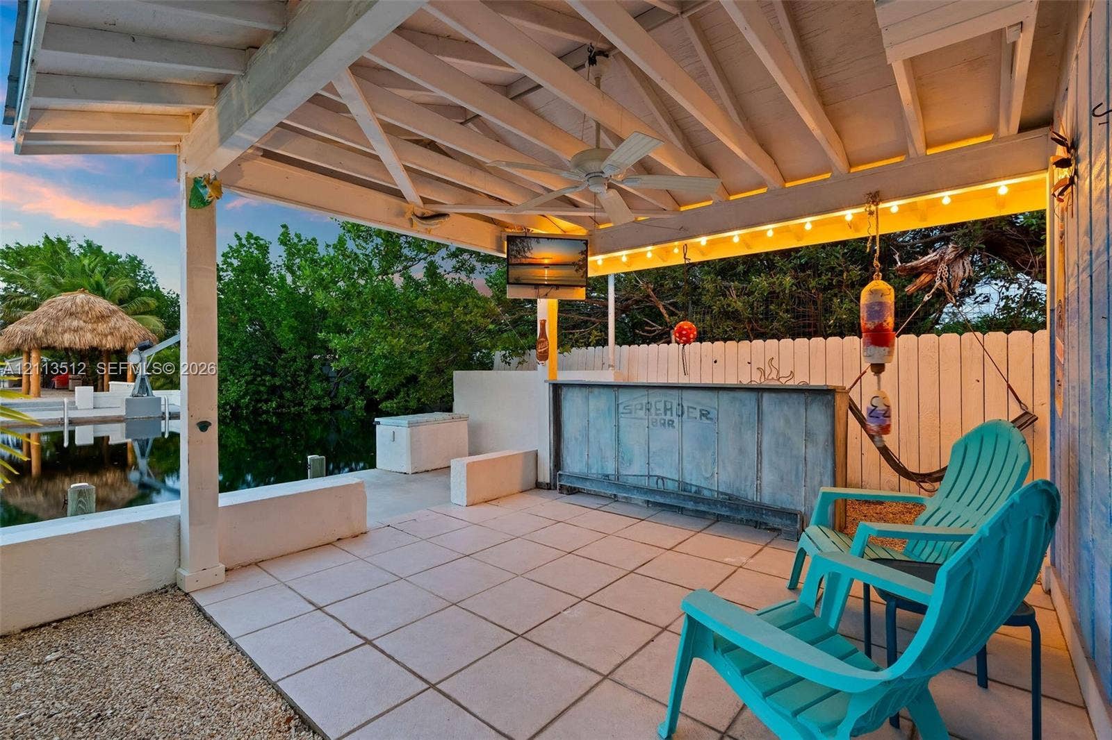 Key Largo, FL 33037 Covered waterfront patio featuring a built-in bar, tile flooring, exposed beamed ceiling with a mounted ceiling fan, and direct access to a concrete seawall