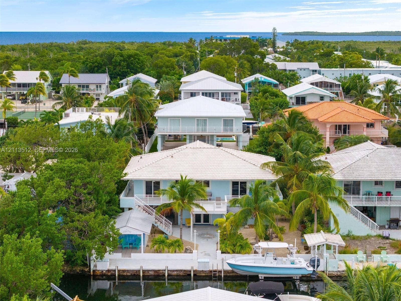 Key Largo, FL 33037 Waterfront residence featuring a private boat dock, elevated deck, light-toned exterior finish, and mature palm trees