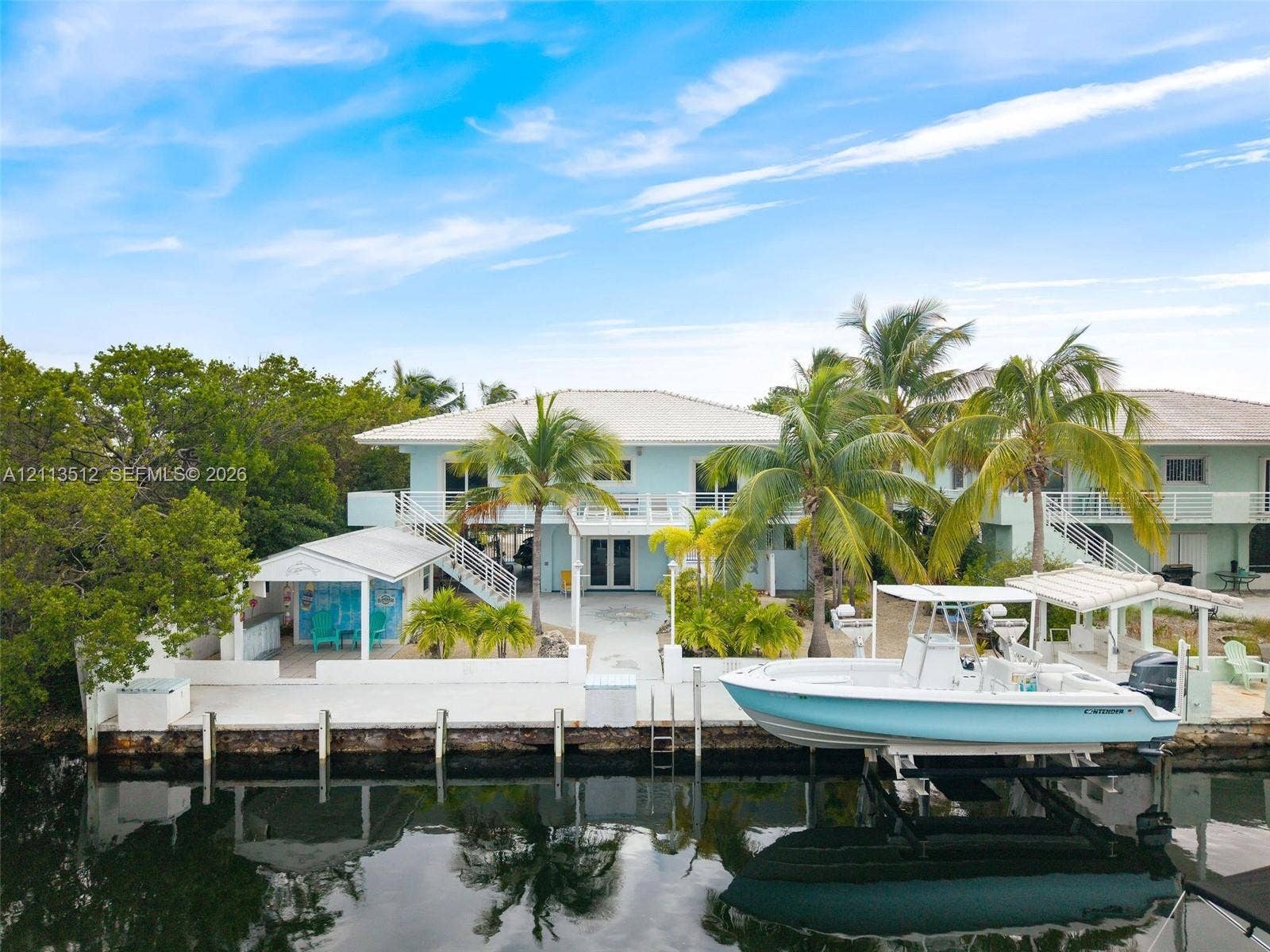 Key Largo, FL 33037 Waterfront property featuring a private boat lift, concrete bulkhead, covered outdoor bar area, and elevated rear deck with staircase access