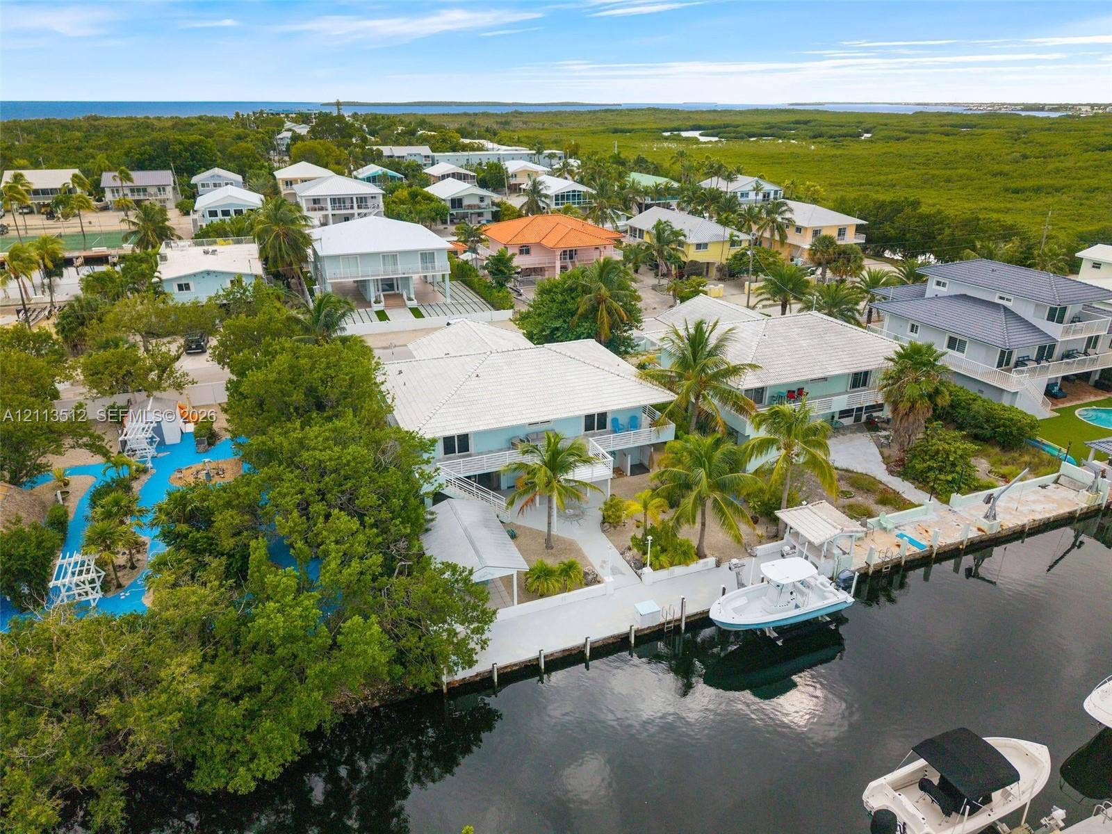 Key Largo, FL 33037 Waterfront property featuring a private boat dock, concrete seawall, tiered tropical landscaping, and mature palm trees