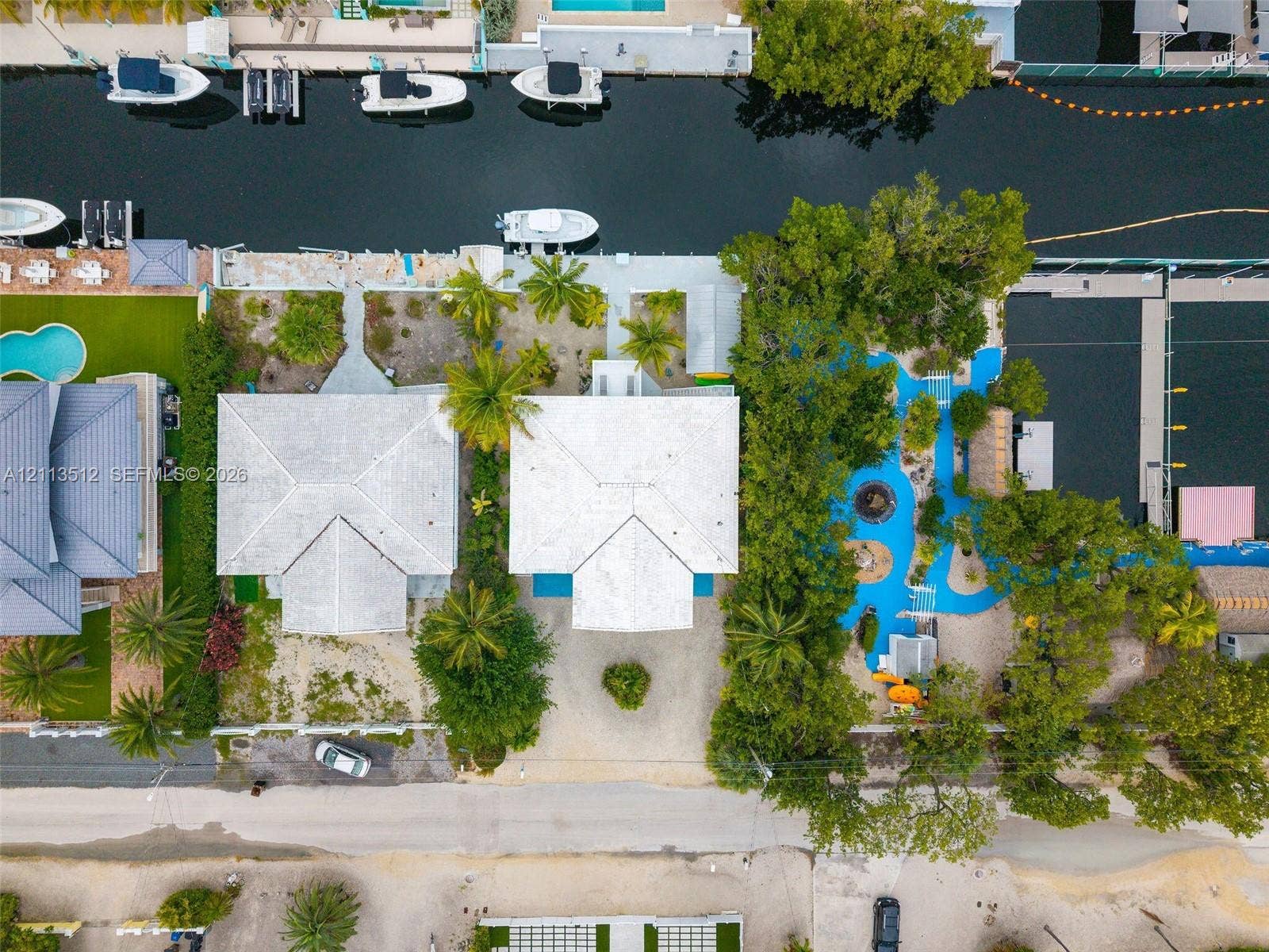 Key Largo, FL 33037 Aerial view of a waterfront property featuring direct canal access, a private boat slip, paved driveway, mature tropical landscaping, and a blue-surfaced outdoor recreation area