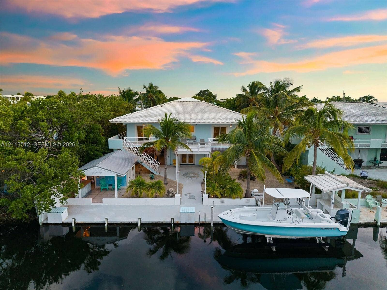 Key Largo, FL 33037 Waterfront residence featuring a private concrete dock, boat lift, expansive ground-level patio, and exterior staircase