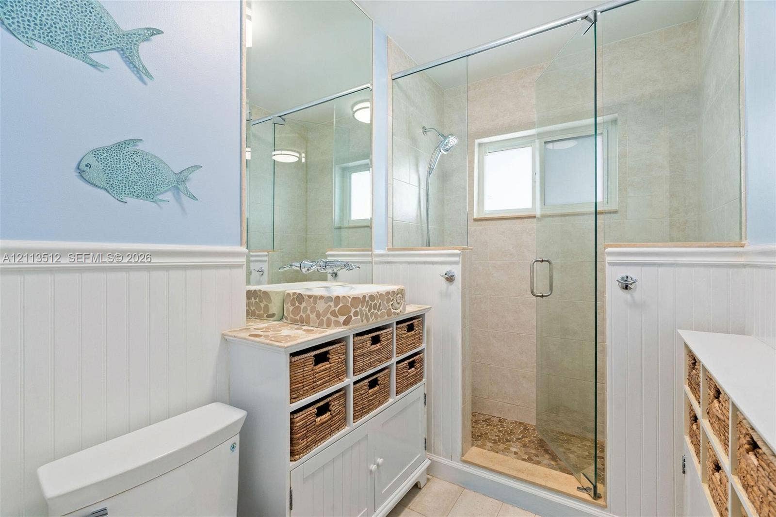 Key Largo, FL 33037 Bathroom featuring a vanity with a stone-accented vessel sink, beadboard wainscoting, glass-enclosed shower, and built-in storage cabinetry