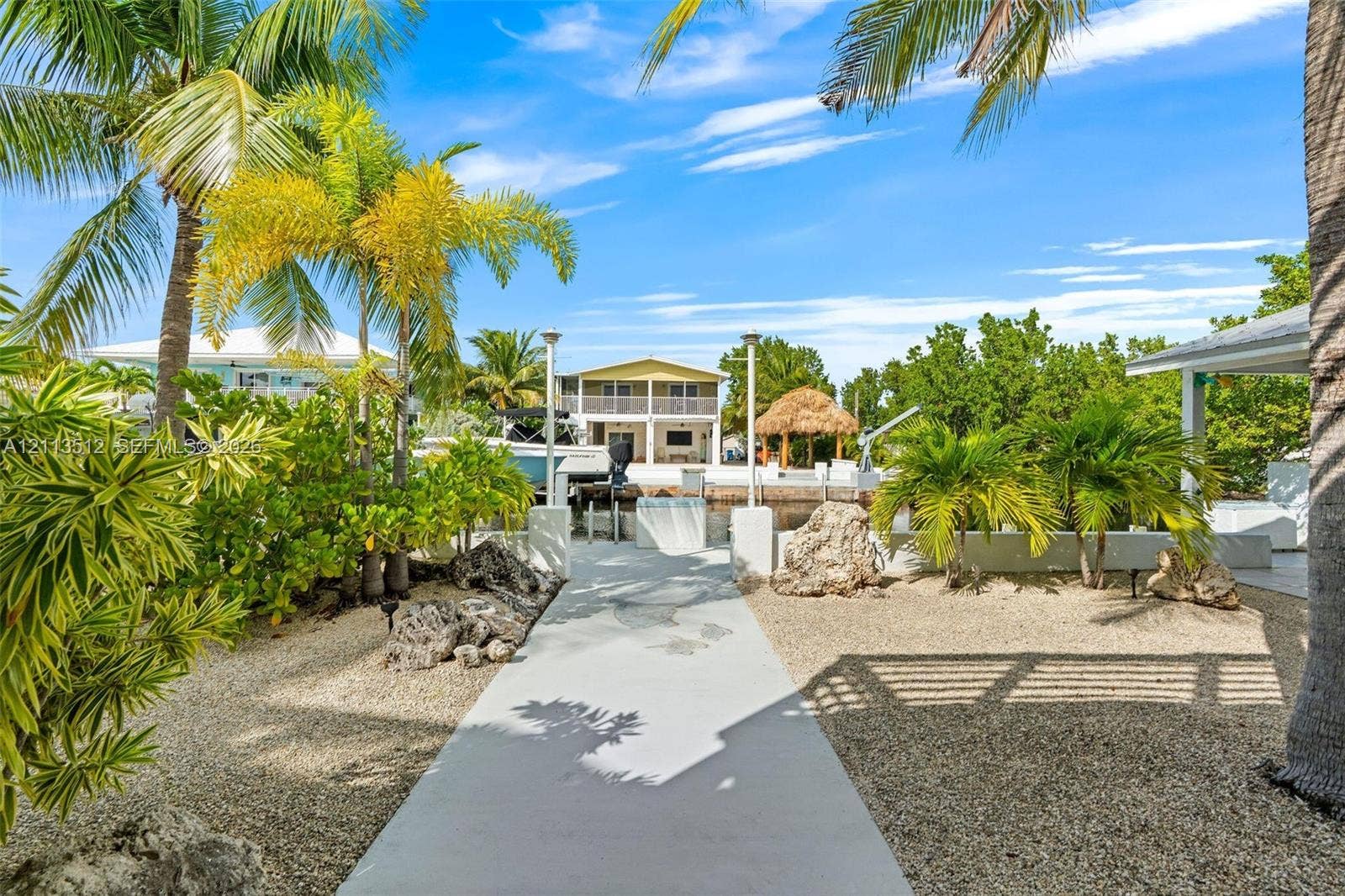 Key Largo, FL 33037 Waterfront property featuring a private boat slip, concrete walkway, gravel landscaping, and mature palm trees