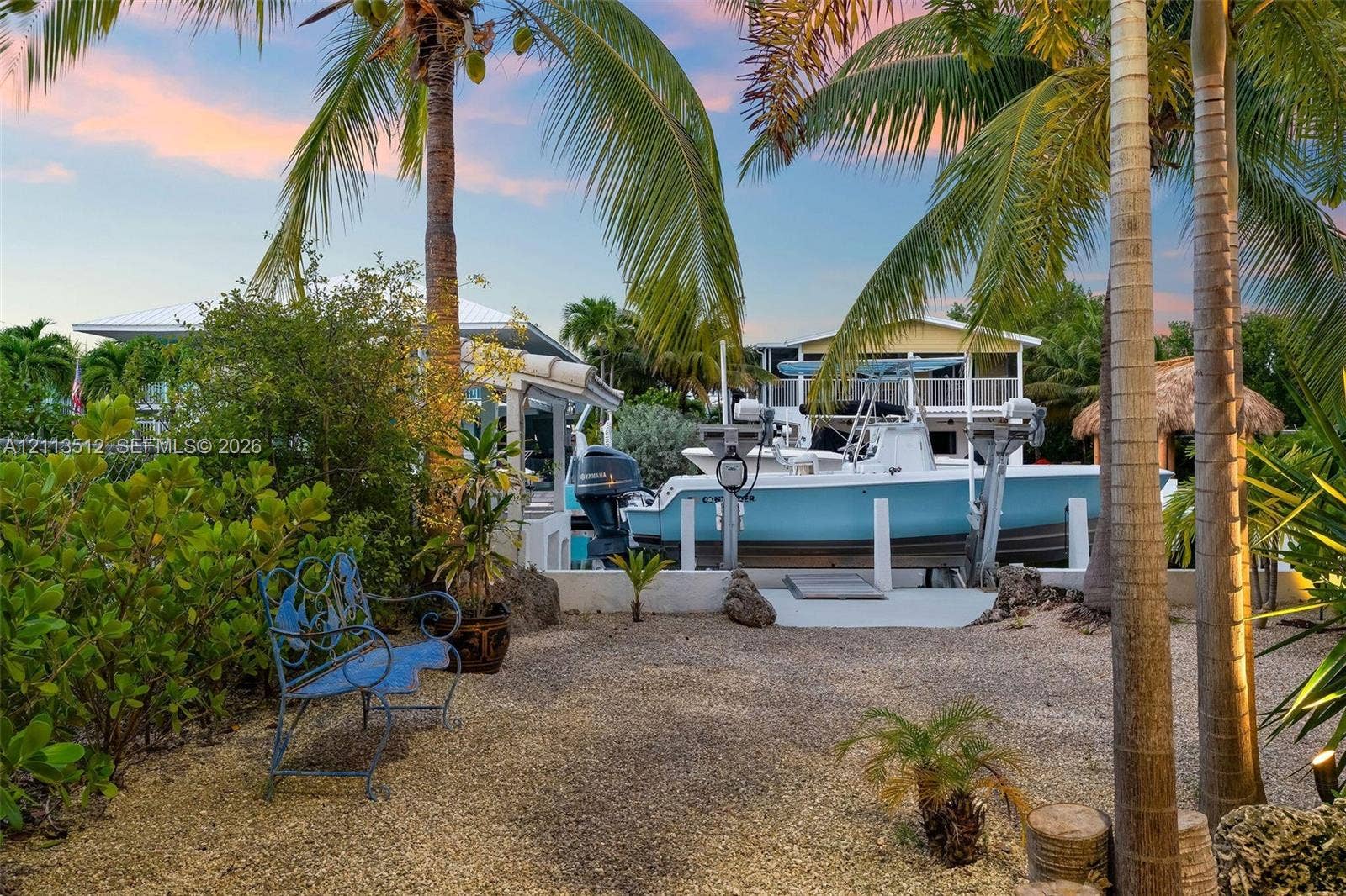 Key Largo, FL 33037 Waterfront property featuring a private boat lift, concrete dock, gravel ground cover, and mature palm trees
